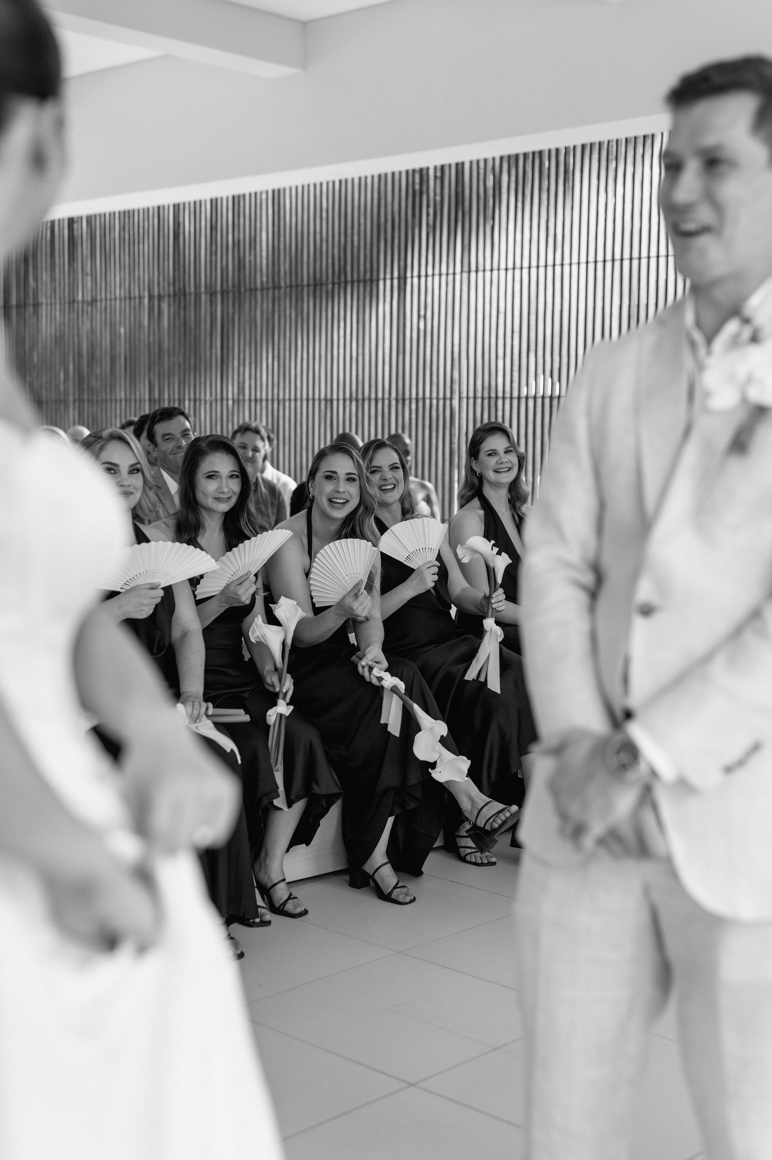 Black and white photo of wedding guests watching ceremony in a modern venue with metallic wall decor.