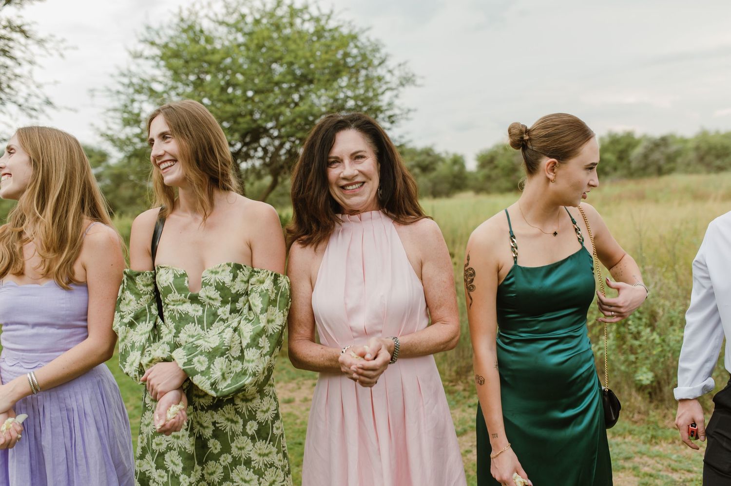 Bridesmaids in pastel and jewel-toned dresses gathered outdoors in a natural setting.