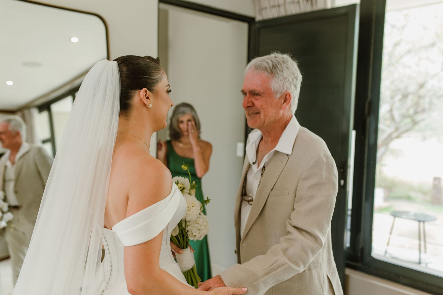 Emotional first look wedding scene in a modern white interior with large windows.