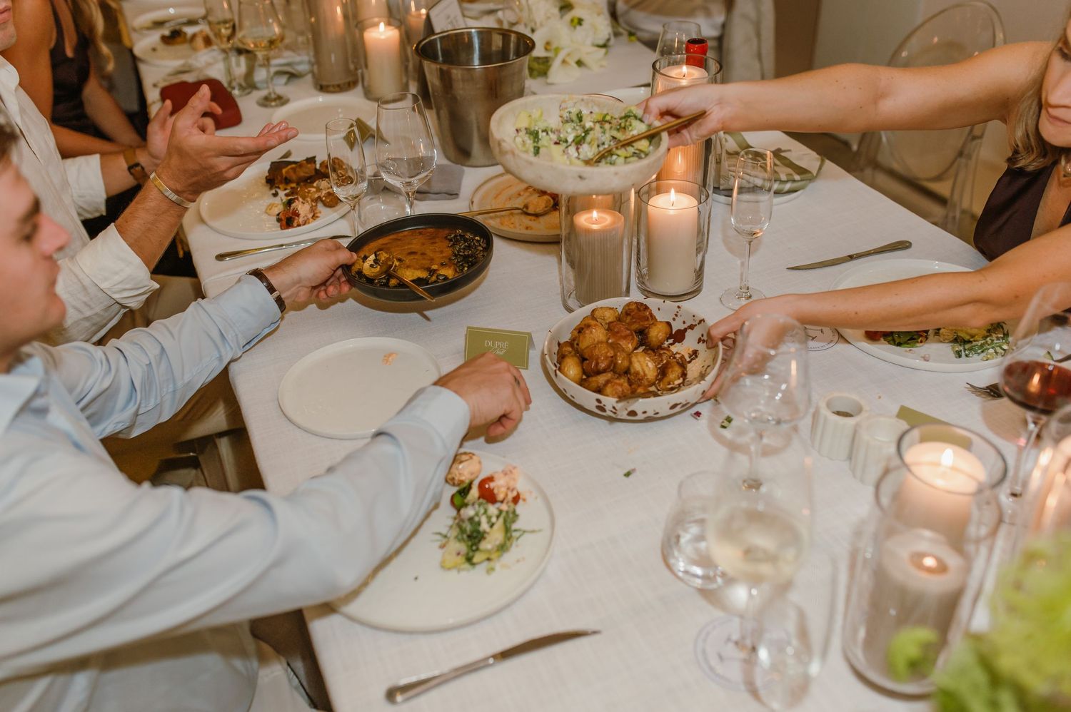Wedding guests sharing plates of food at an elegantly set reception dinner table.