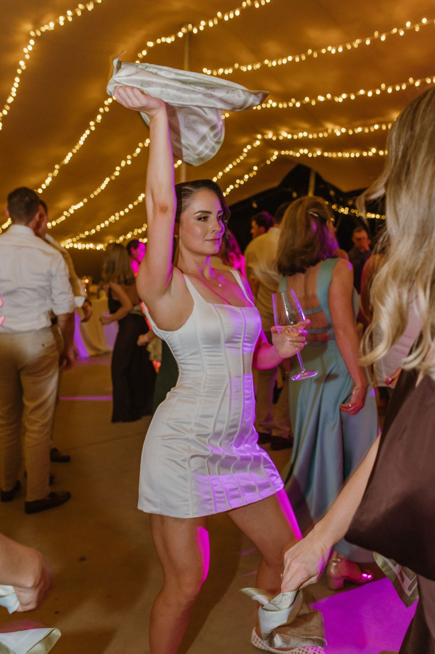 Wedding guests dancing and celebrating under colorful lights and string light decorations.