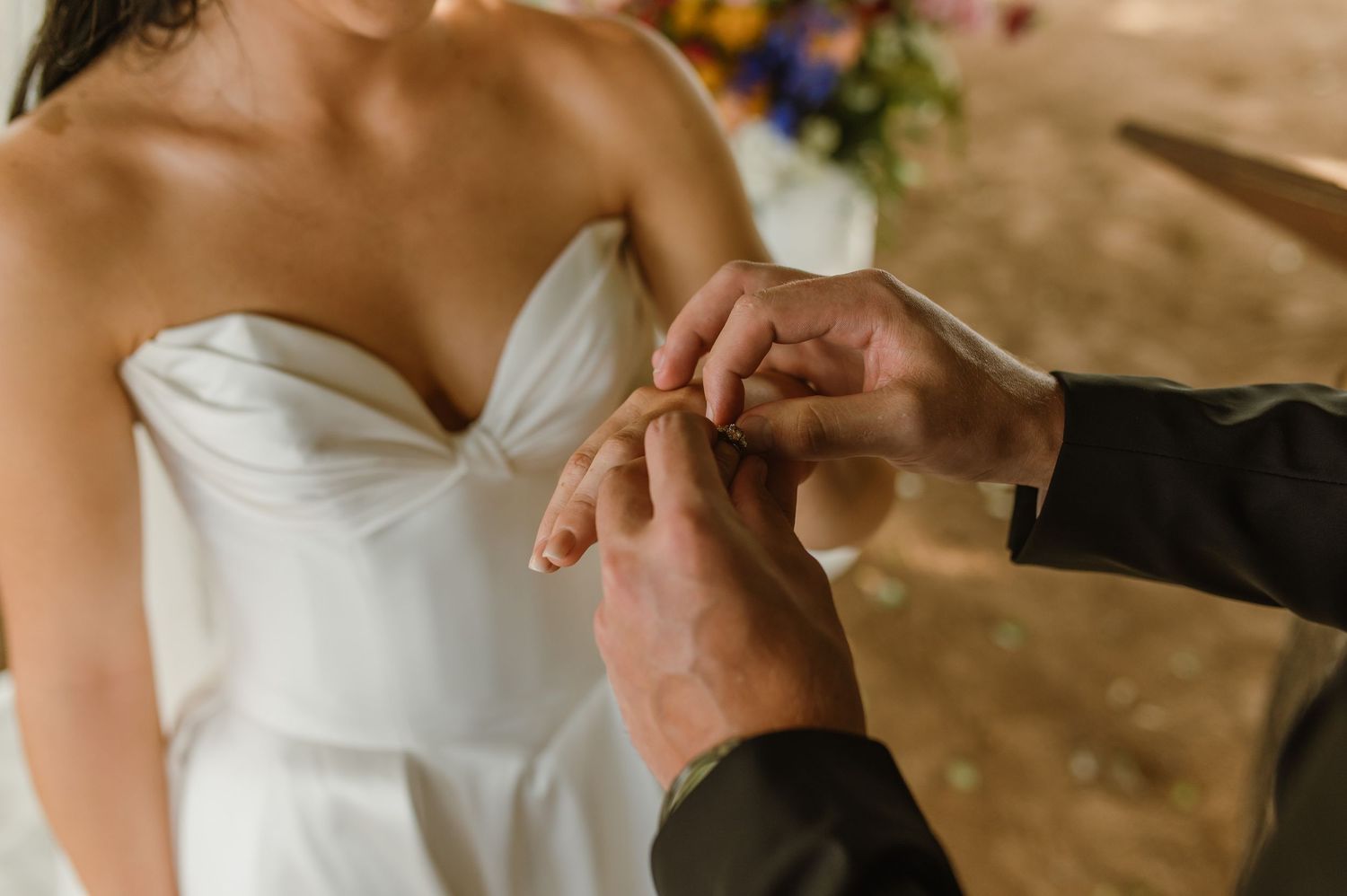 Close-up of groom placing wedding ring on brides finger during outdoor ceremony.