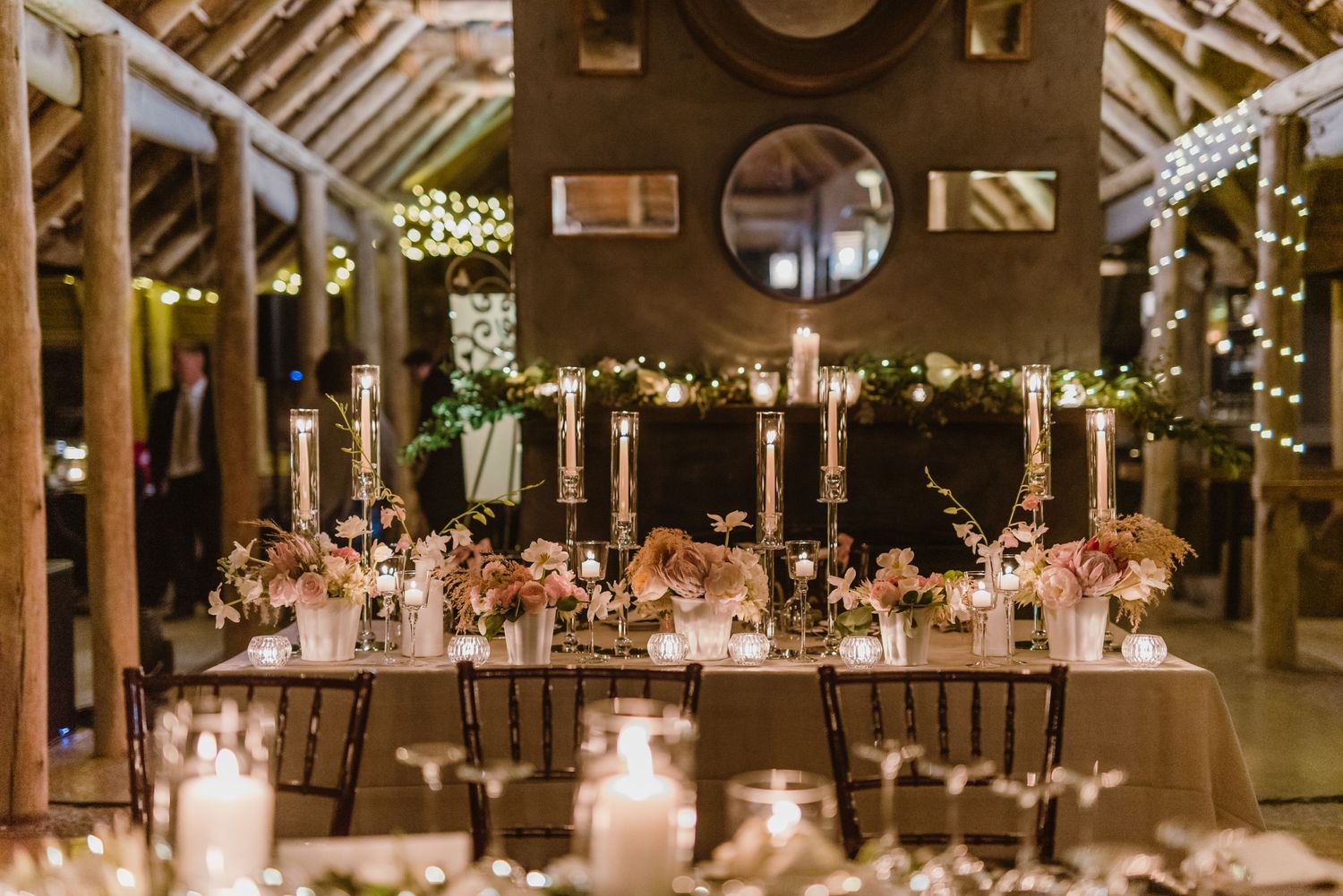 Elegant wedding reception hall with long tables and ambient lighting under exposed wooden beams.