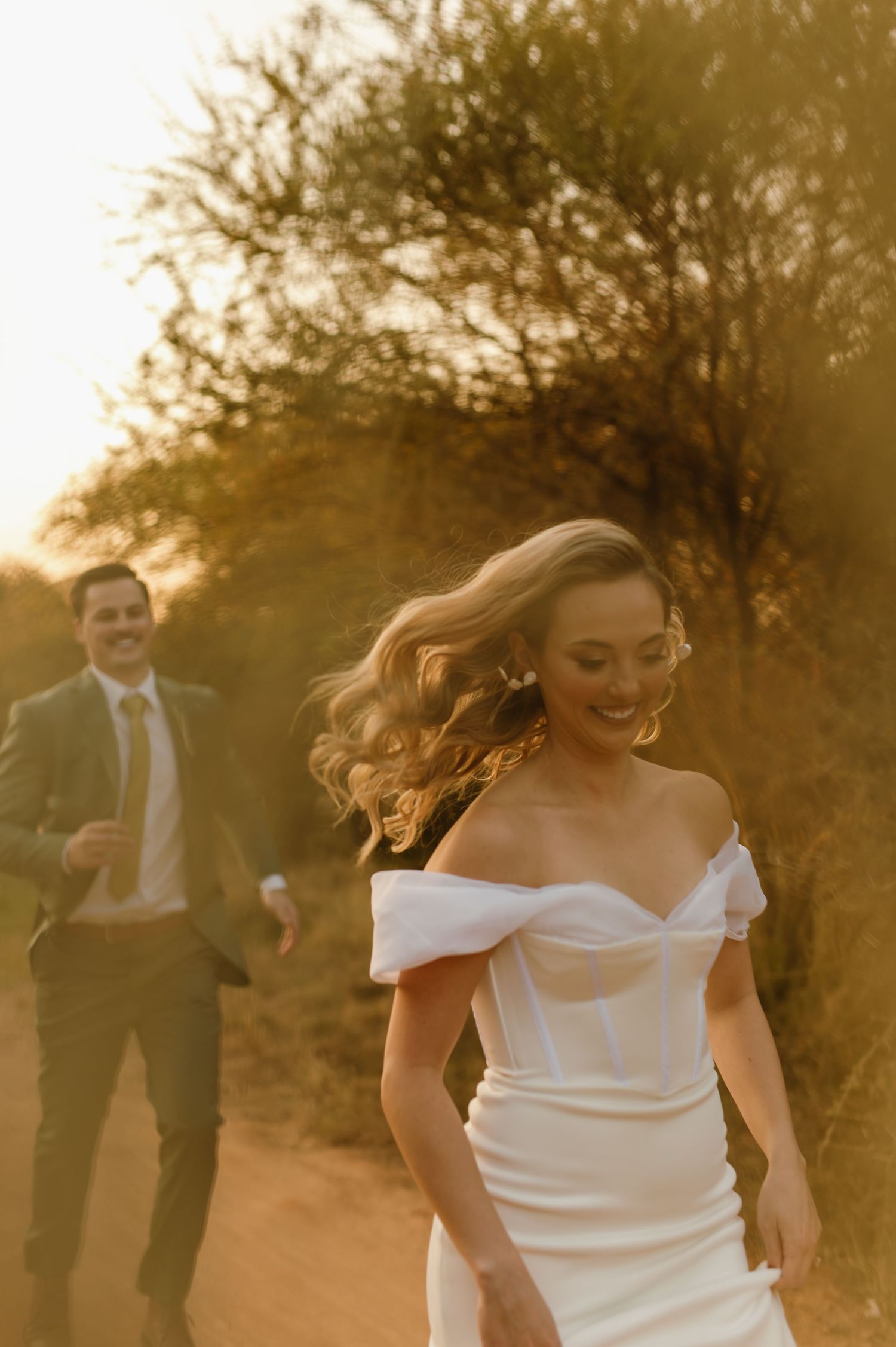 Candid moments of a bride in white dress dancing on a dusty path at sunset.