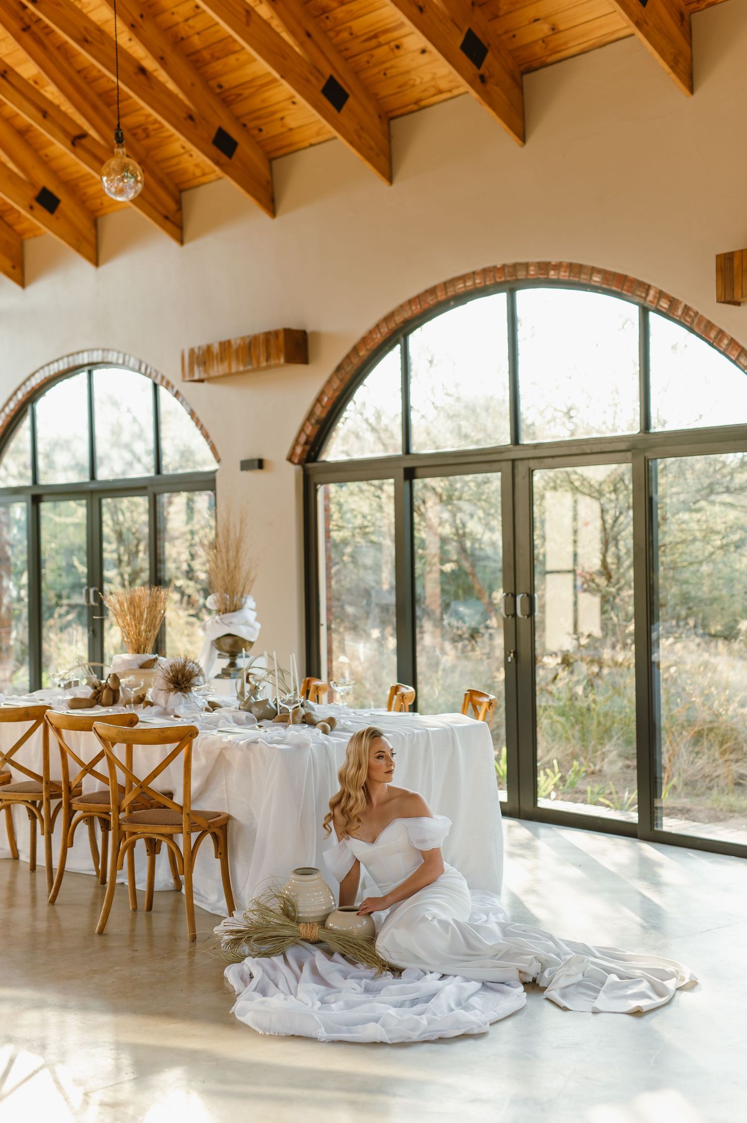 Modern wedding venue with wooden beam ceiling, arched windows, and elegant table settings.