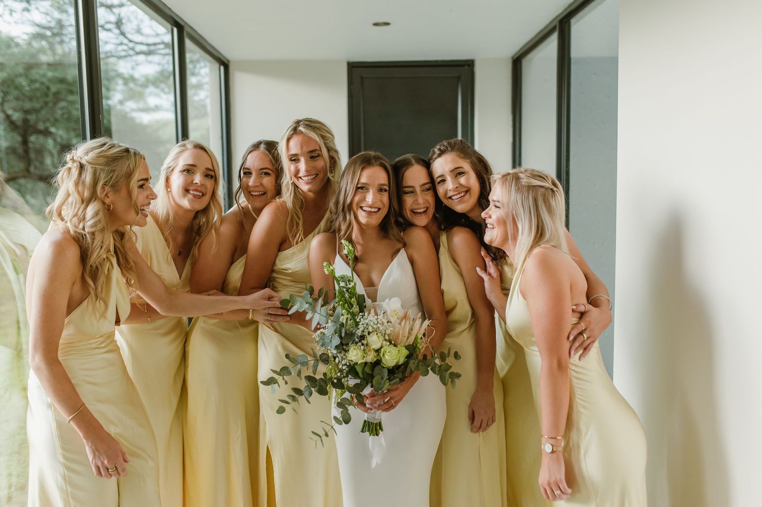 Wedding party in coordinated yellow and white dresses posing in modern interior.