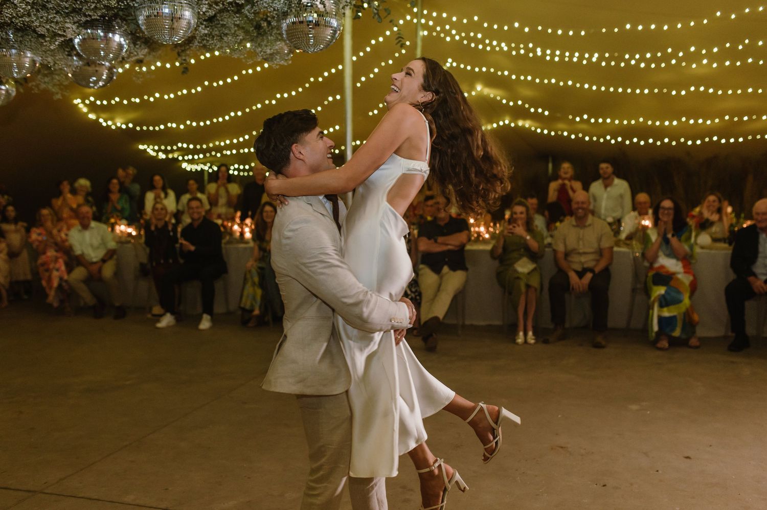 A joyful dance lift moment during a wedding reception under warm string lights.