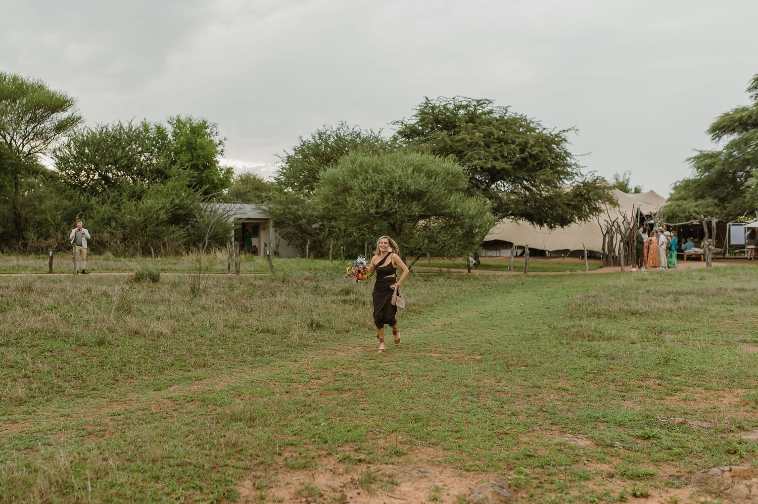 Wedding party members walk across a grassy field during an outdoor celebration.