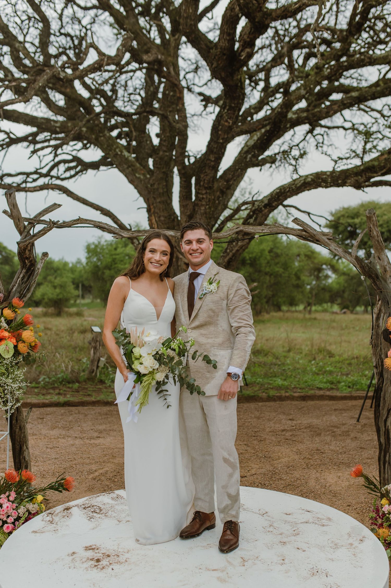 Outdoor wedding portraits under a majestic tree with white and orange floral decorations.
