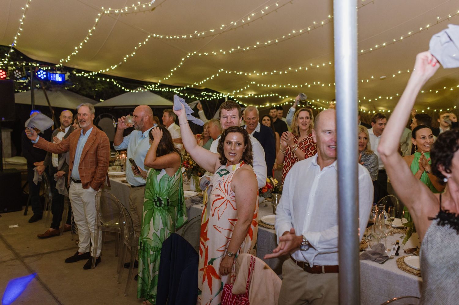 Guests enjoy dancing at a wedding reception under warm string light decorations.