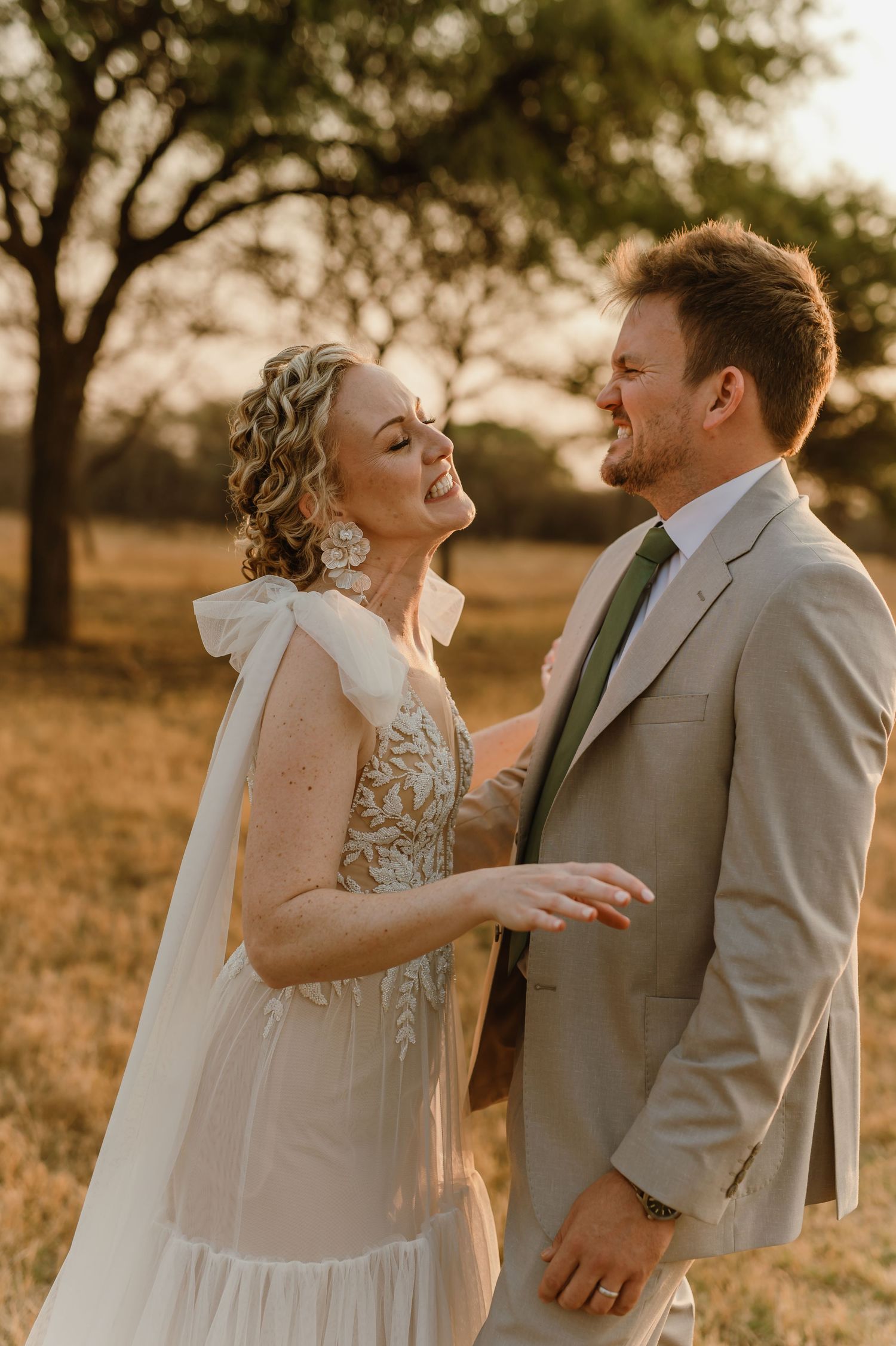 A wedding couple shares a joyful moment in a sun-drenched field during golden hour.
