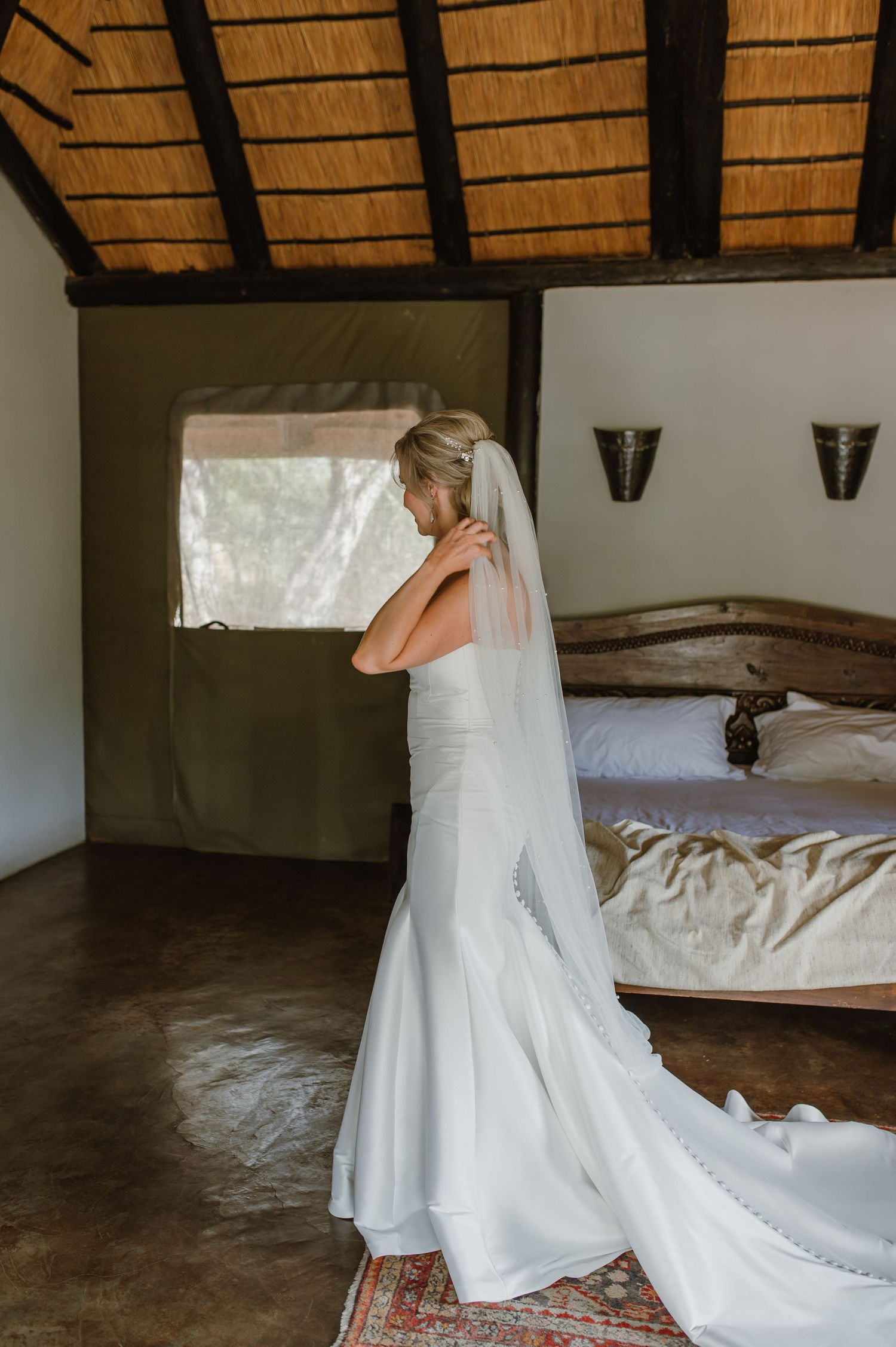 Flowing white wedding dress train on concrete floor under thatched roof.
