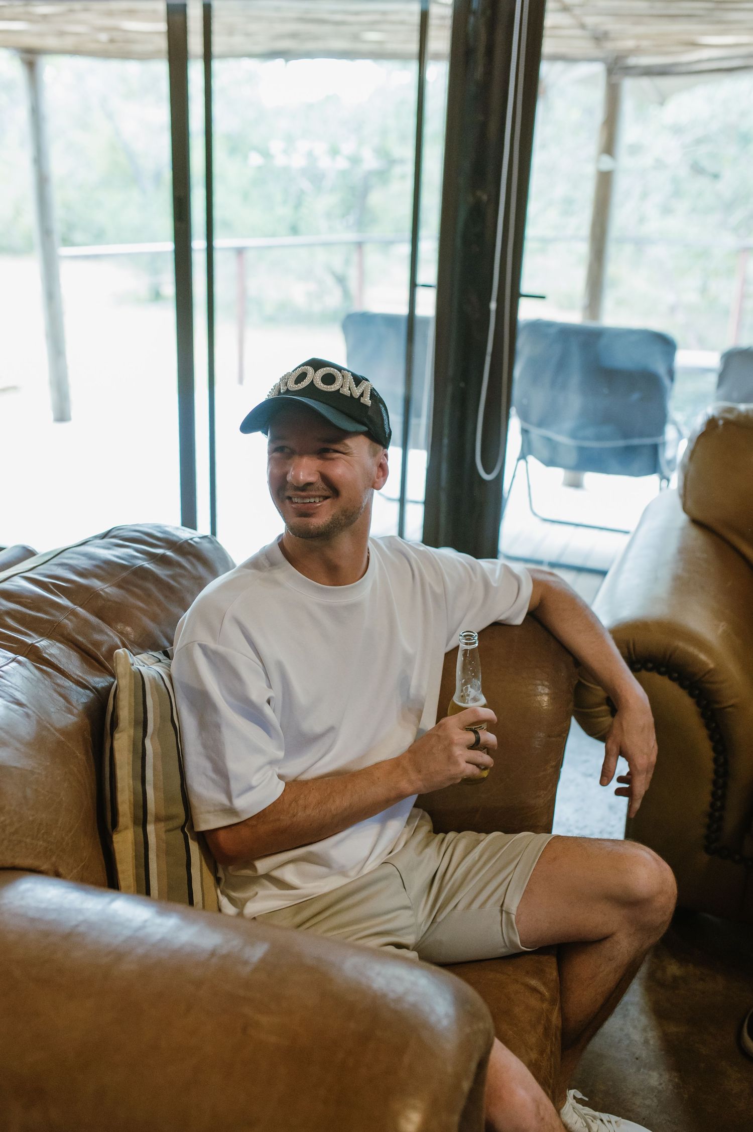 Person relaxing on brown leather couch in sunlit room with exposed wooden beams.