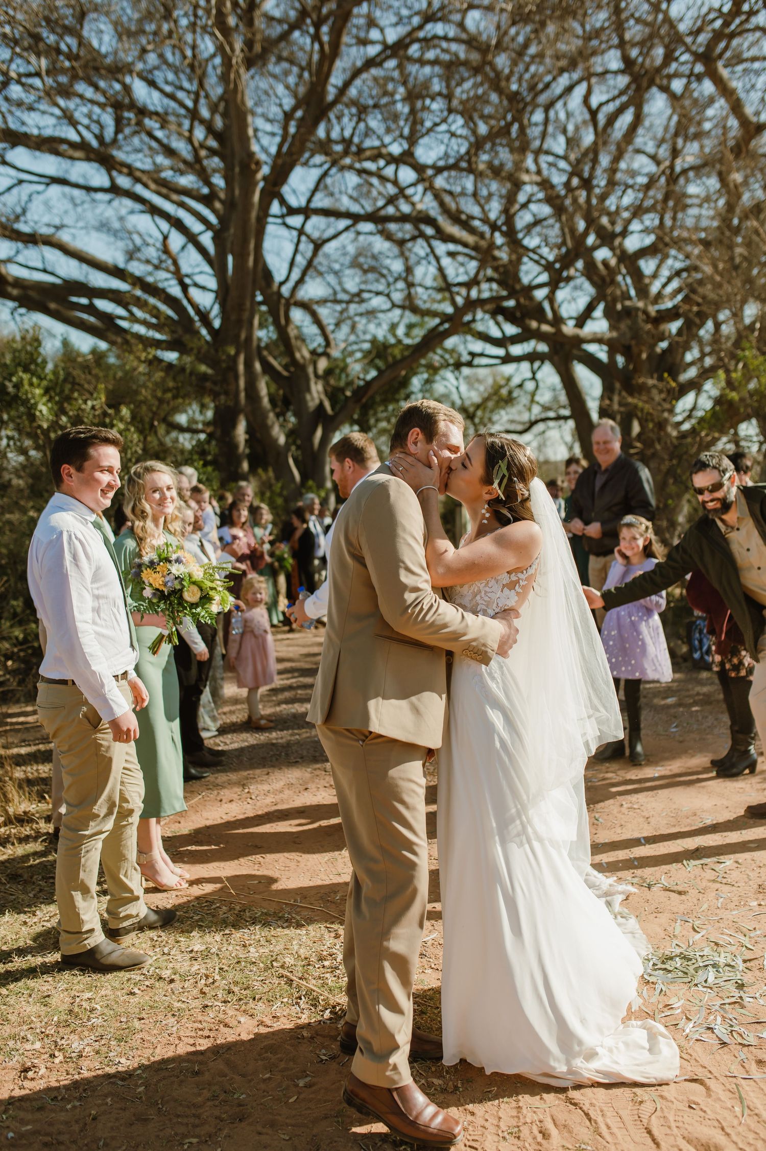 Wedding ceremony in a natural setting with guests watching among twisted oak trees.
