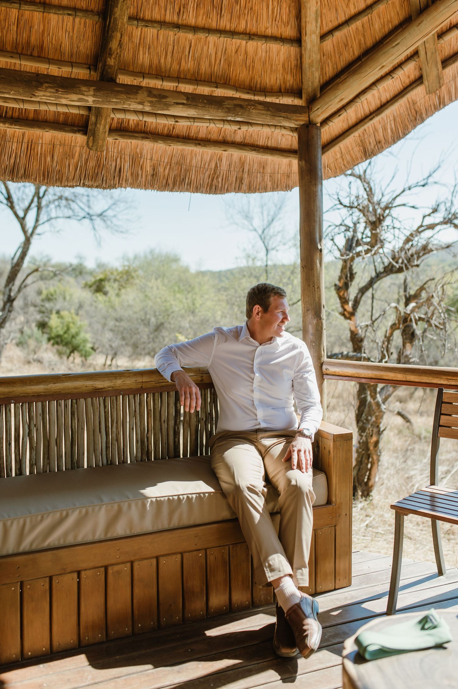 Person in white shirt relaxing in a thatched-roof gazebo with scenic mountain views.