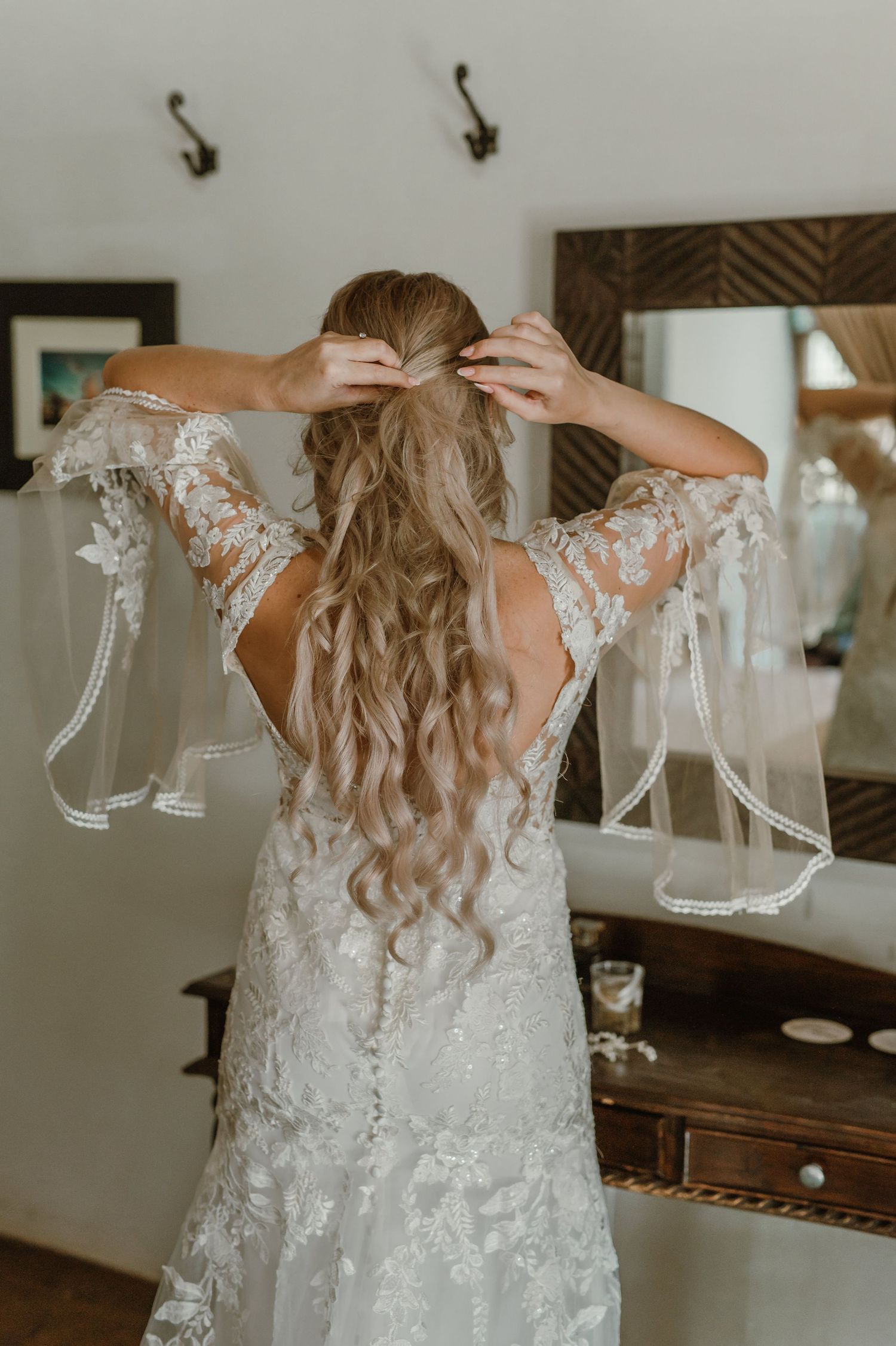 Back view of a wedding dress showing intricate lace details and long wavy hair.