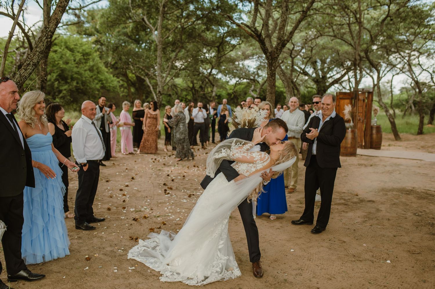 Outdoor wedding ceremony with guests watching under natural tree canopy.