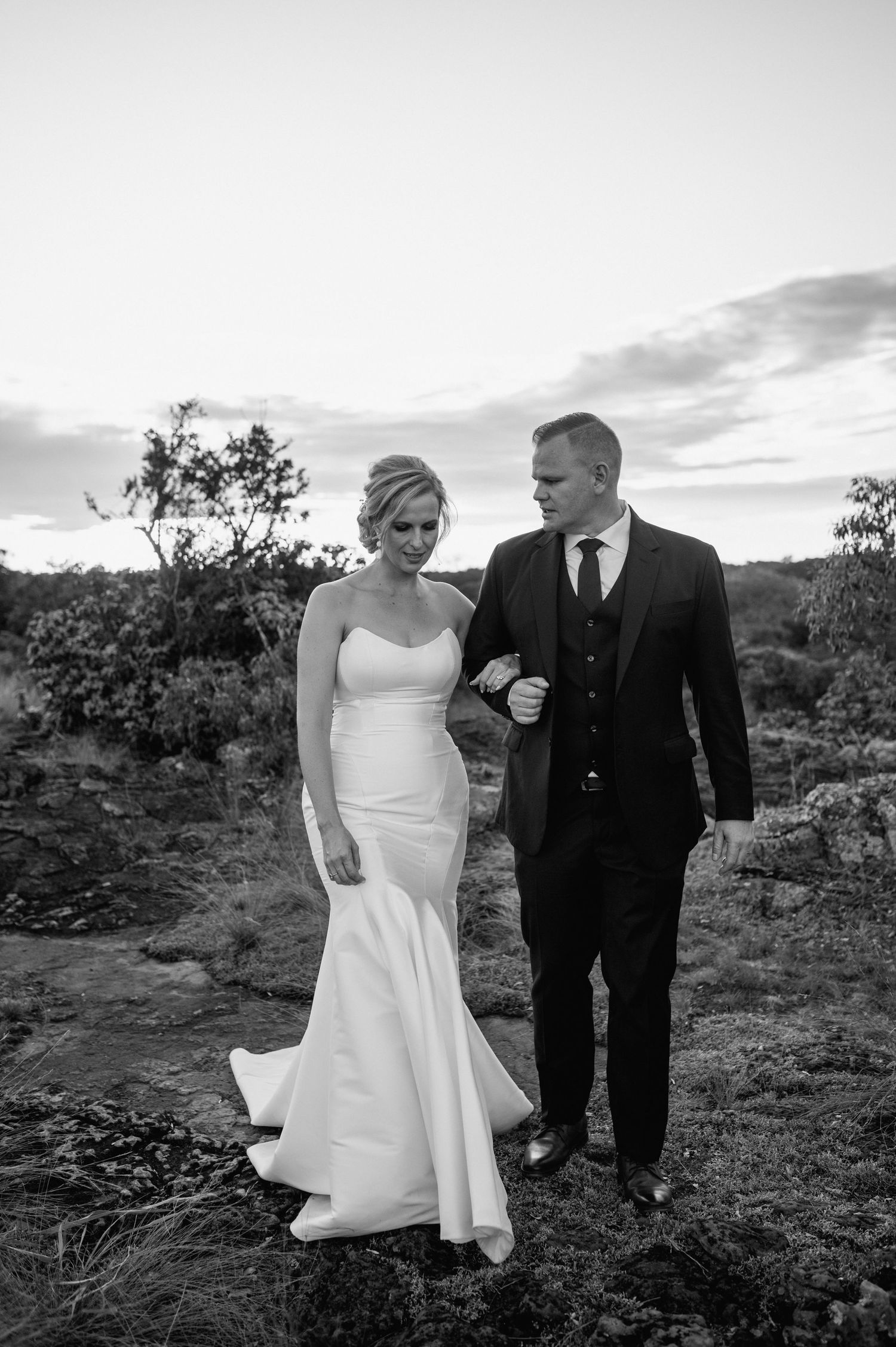 Black and white wedding portrait shows couple walking through desert landscape.