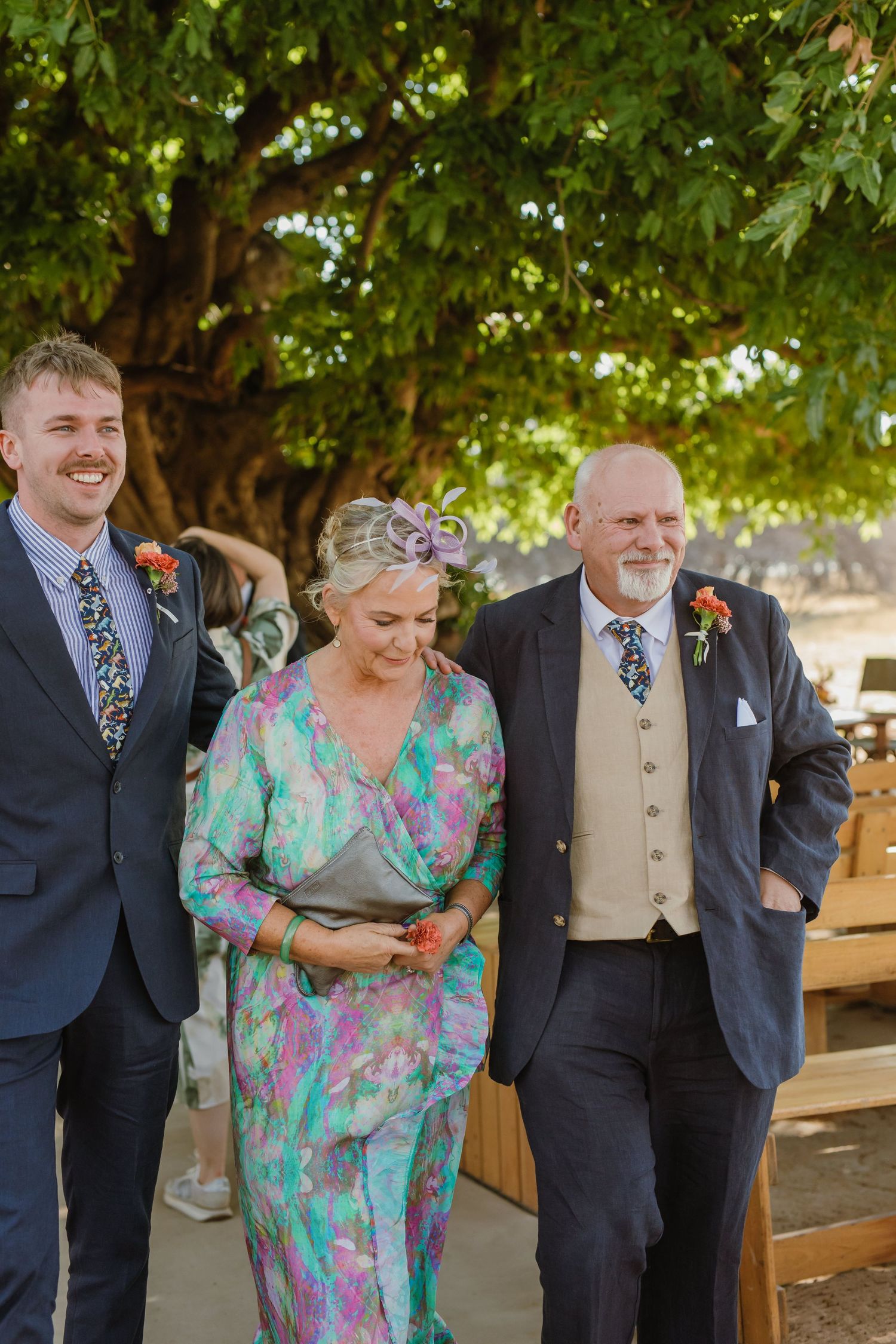 Wedding guests in colorful attire laugh together during outdoor celebration.