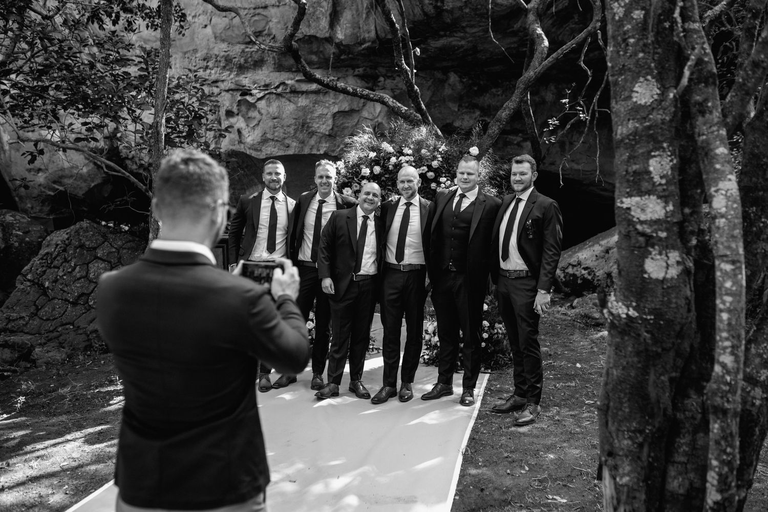 Black and white photo of wedding guests gathering outdoors under trees.