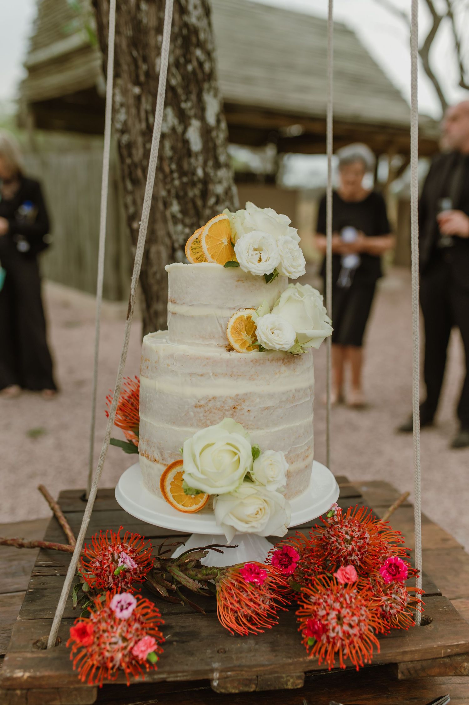 Elegant white wedding cake decorated with fresh flowers and dried orange slices on rustic wooden table.
