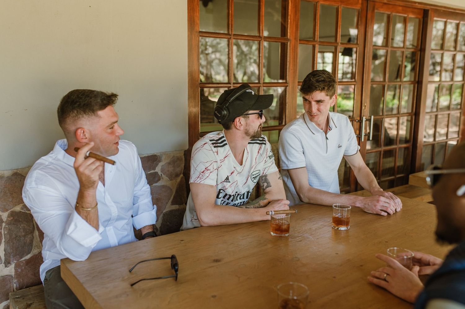 Friends gather around wooden table for drinks and conversation at outdoor venue.