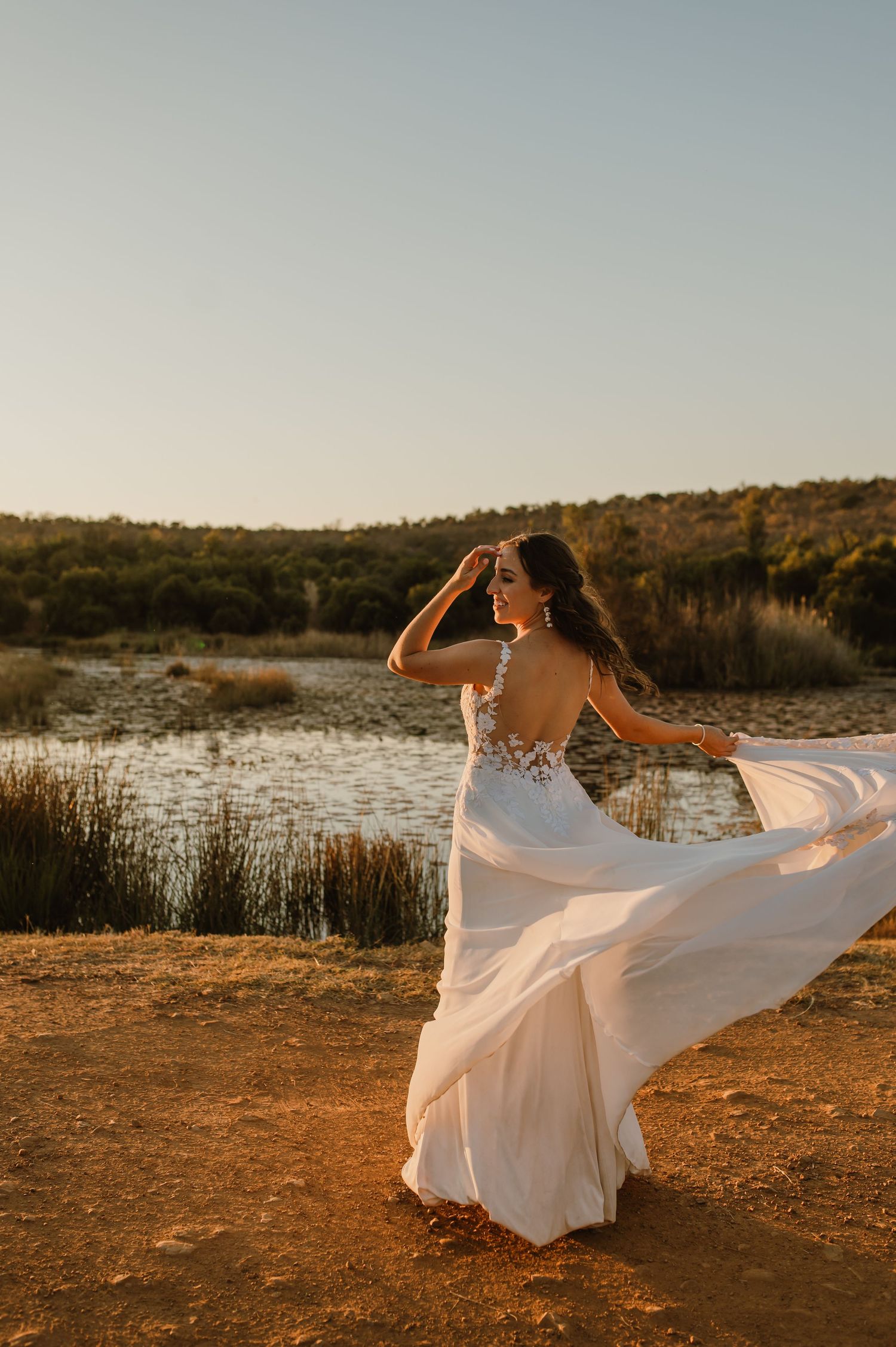 A bride spins in her white wedding dress during golden hour on a hilltop overlooking nature.