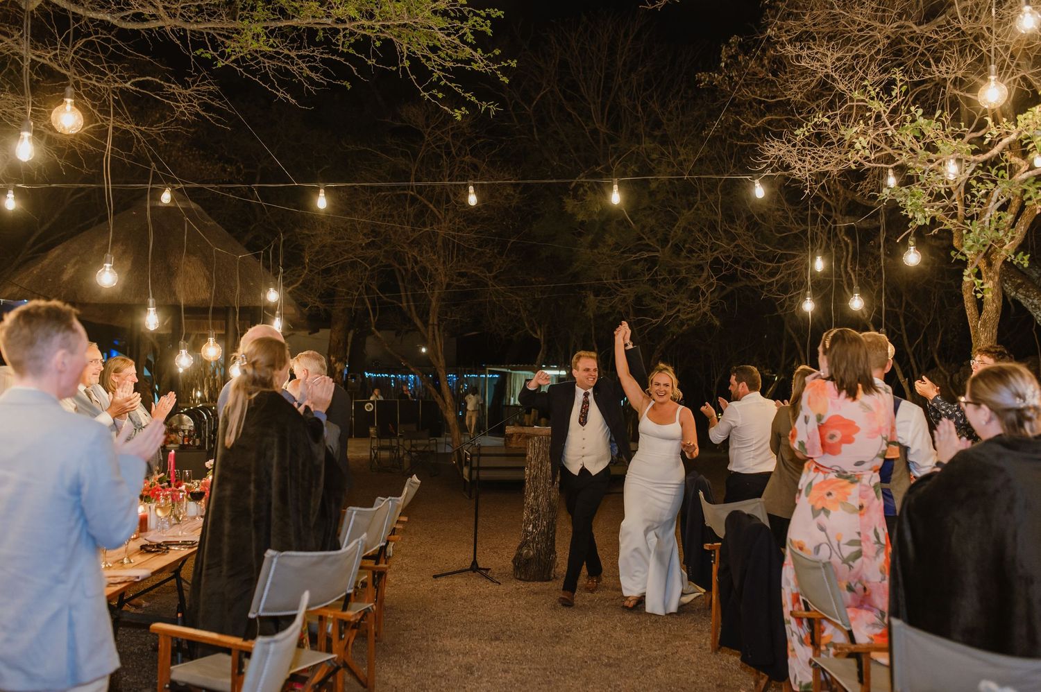 Festive outdoor gathering with string lights illuminating guests and tables in evening setting.