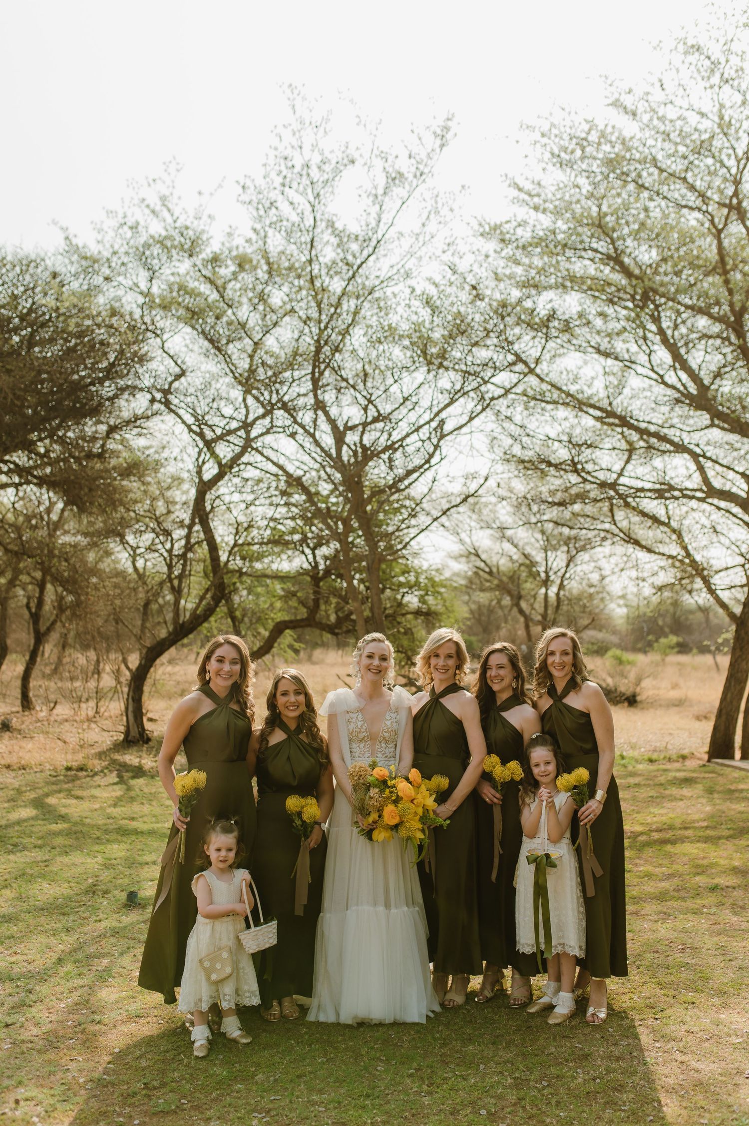 Wedding party with bright sunflower bouquets poses together outdoors against natural landscape.
