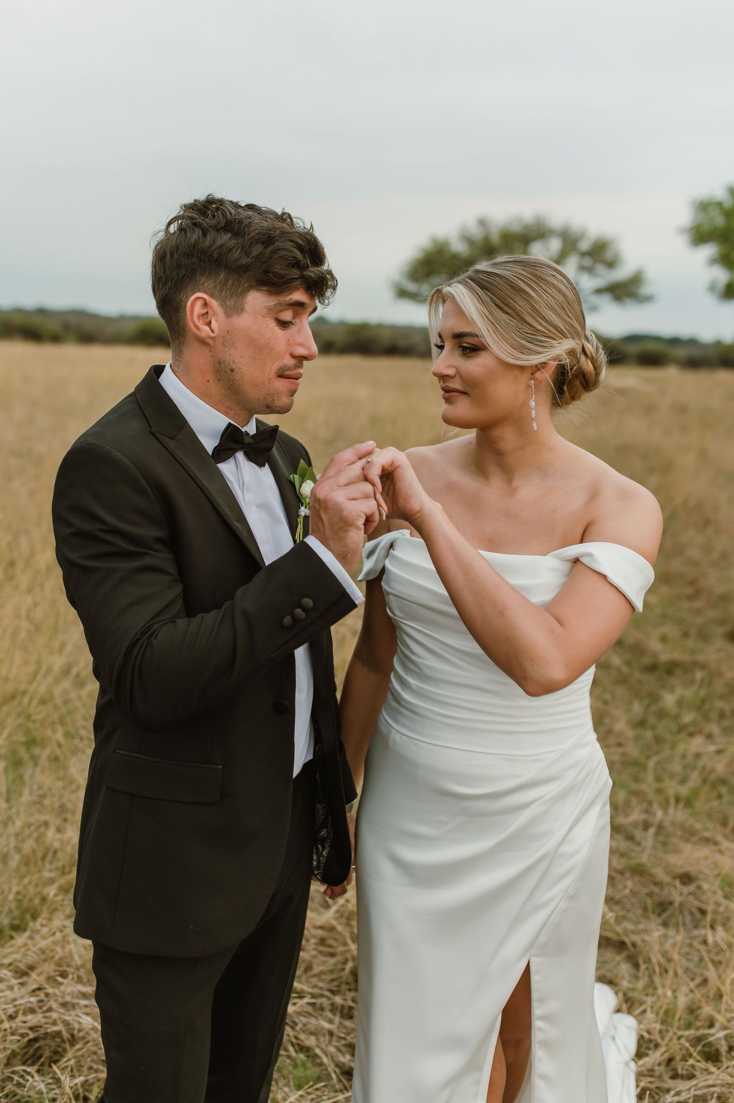 A couple shares romantic gestures during their wedding photoshoot in a natural grassland setting.