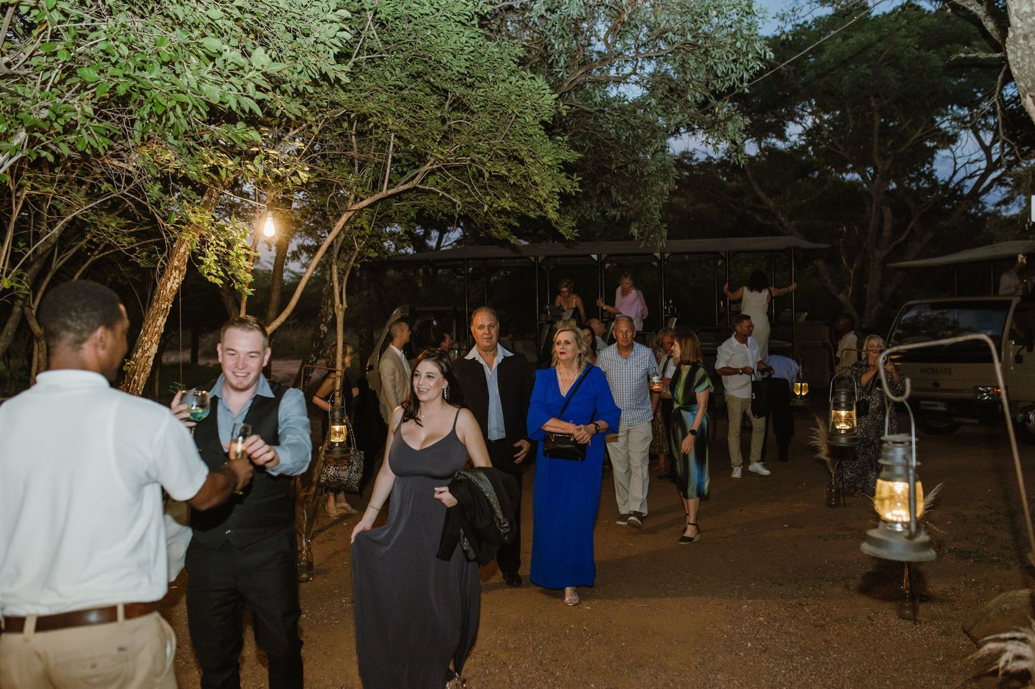 Evening outdoor celebration with guests mingling under string lights and trees.