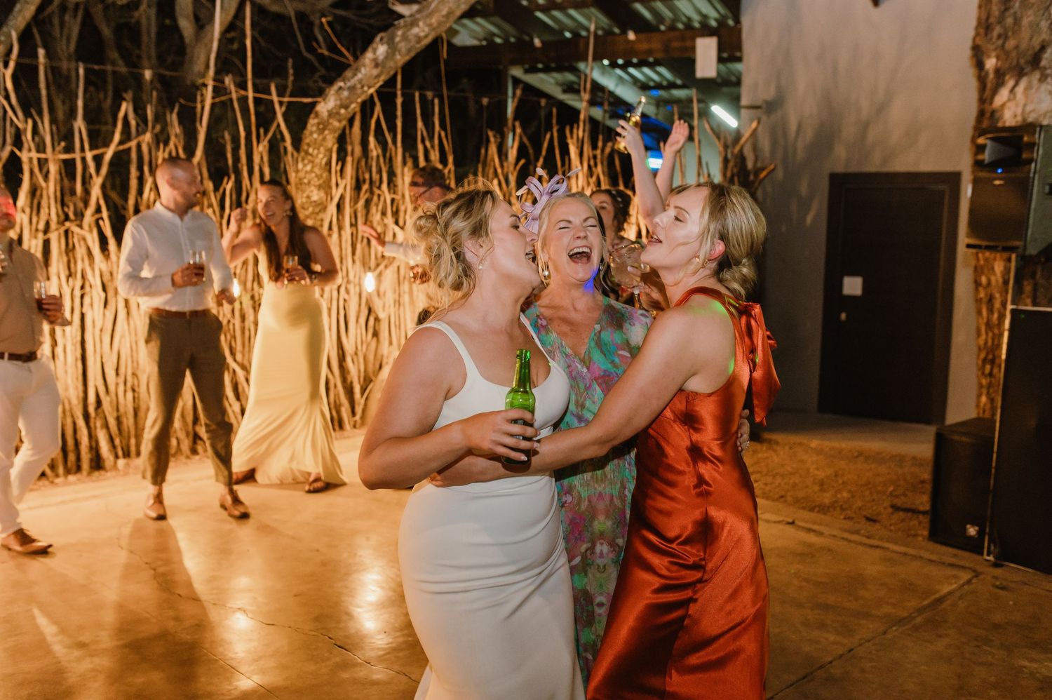 Wedding celebration with guests dancing and laughing in rustic venue with ambient lighting.