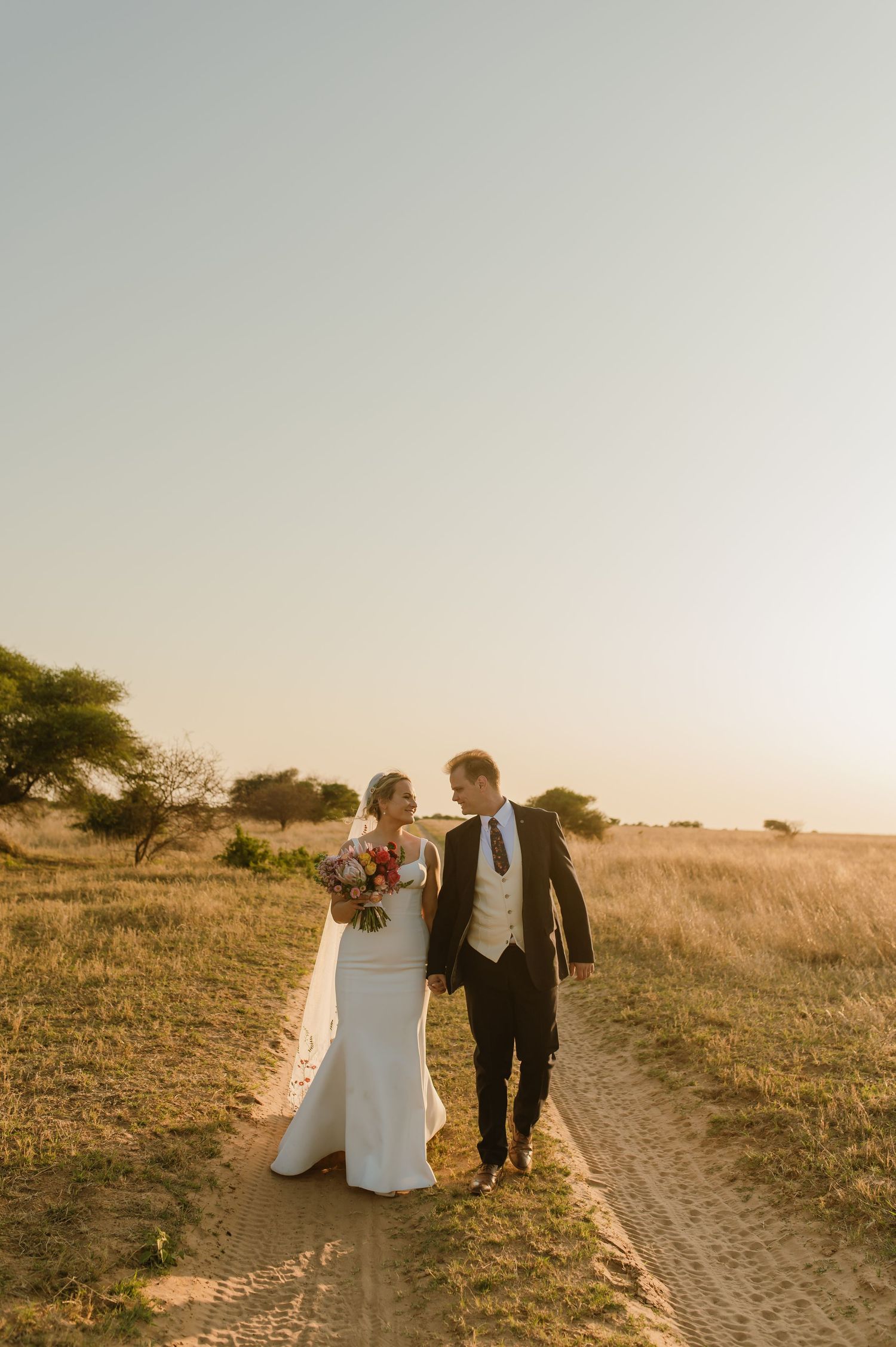 Romantic sunset wedding photos of couple walking along dirt path in golden light.