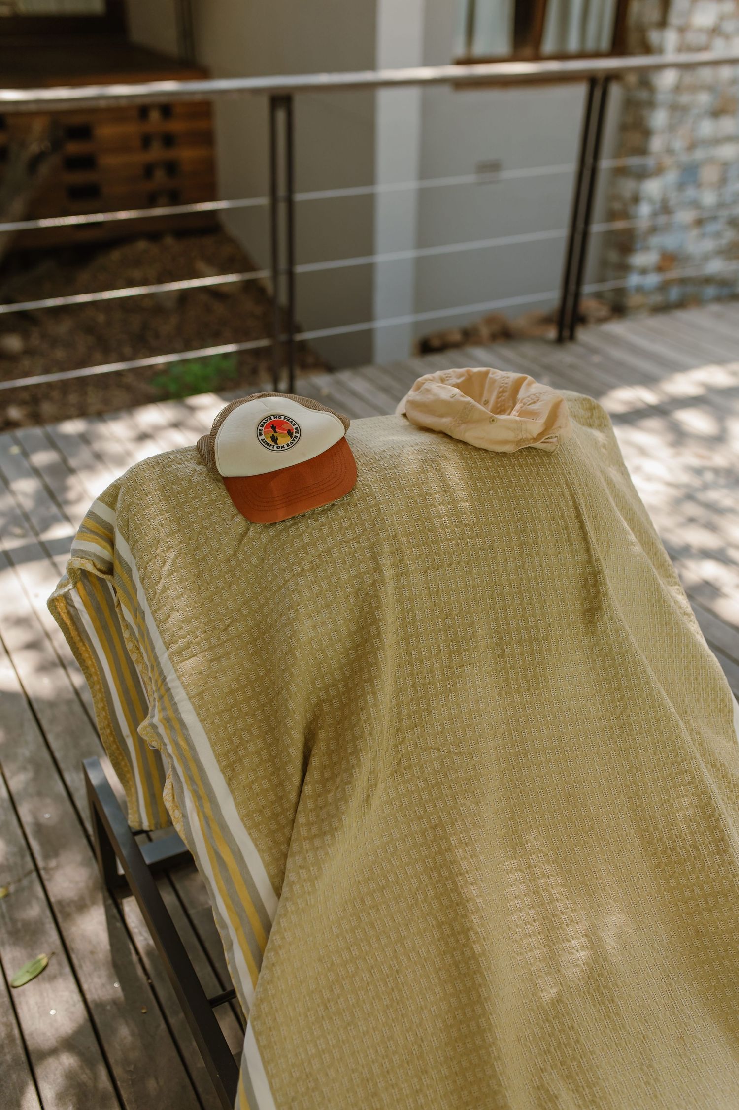 Yellow waffle towel and orange trucker hat on a striped lounge chair outdoors.