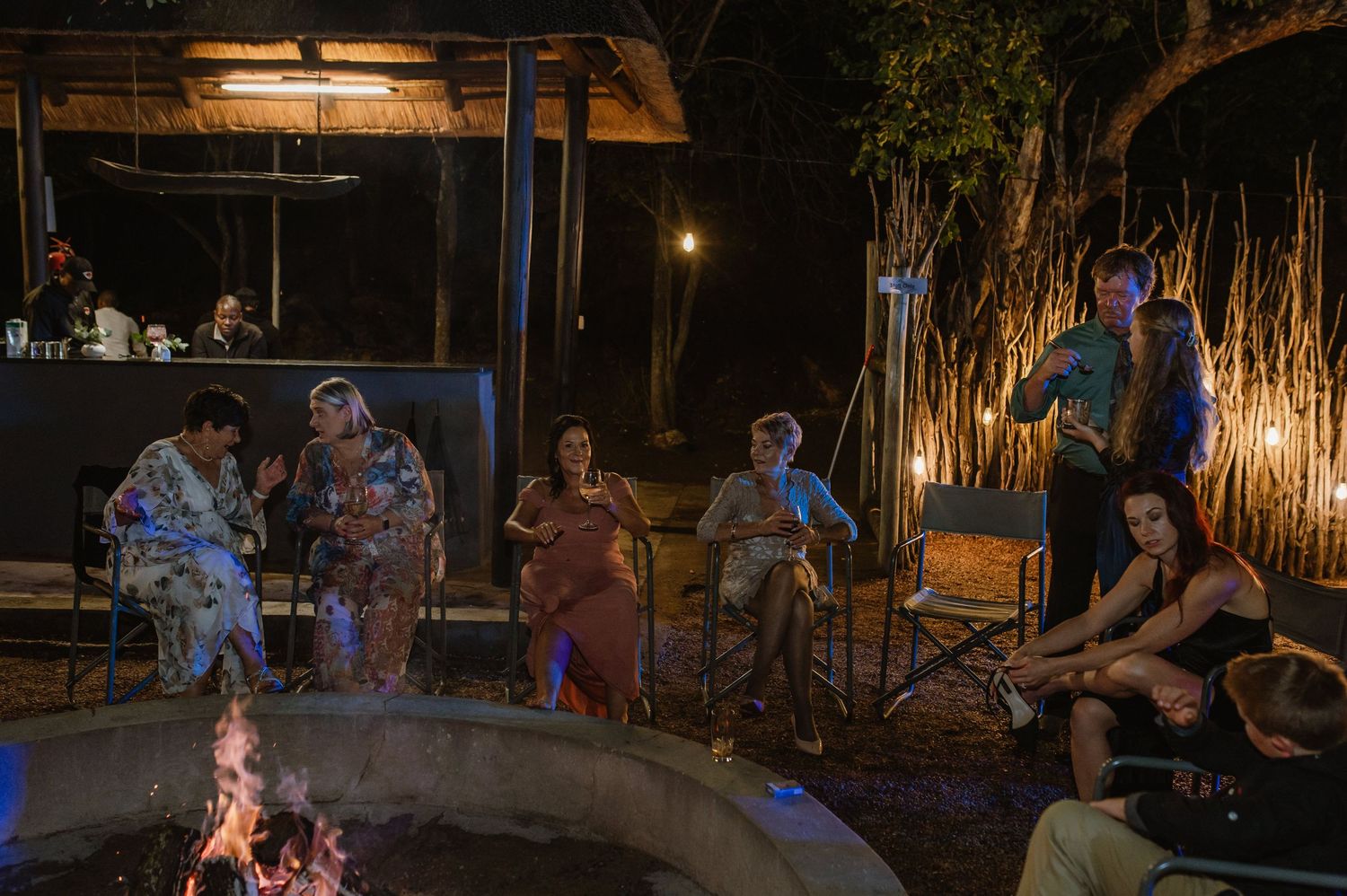 Wedding guests gather around a glowing fire pit for an intimate outdoor evening celebration.