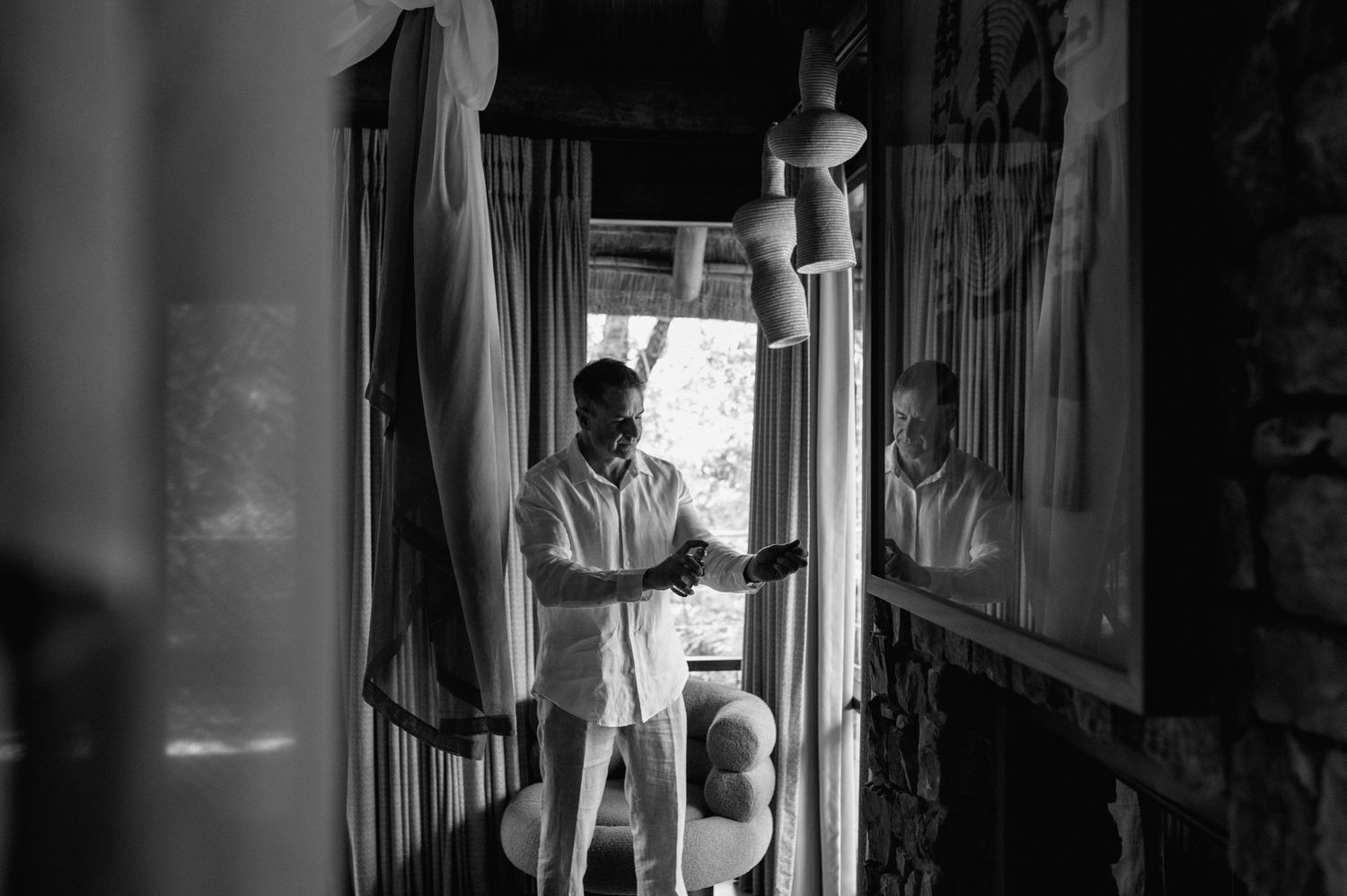 Groom getting ready in black and white photo standing by window with balloons in rustic room.