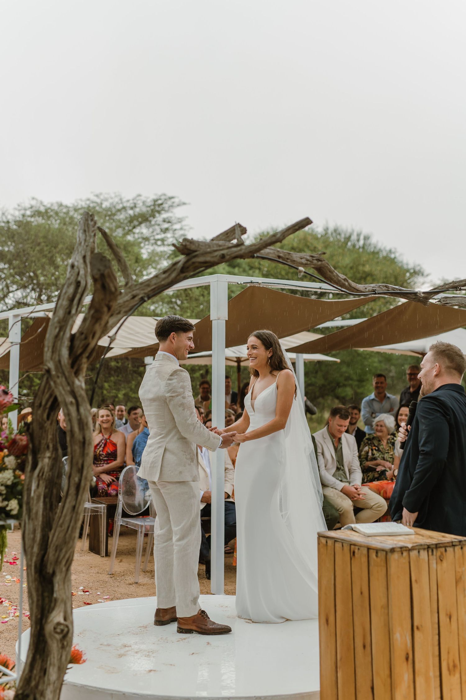Wedding ceremony setup with white pergola and wooden details in a natural desert setting.