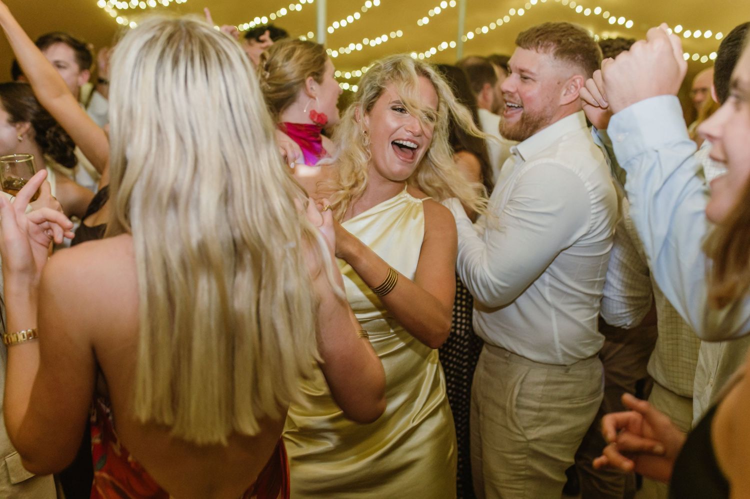 Lively dance floor scene with wedding guests celebrating under decorative lighting.