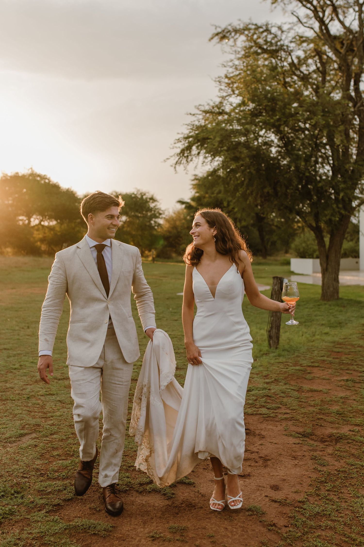 A couple walks together on a dirt path during golden hour in wedding attire.