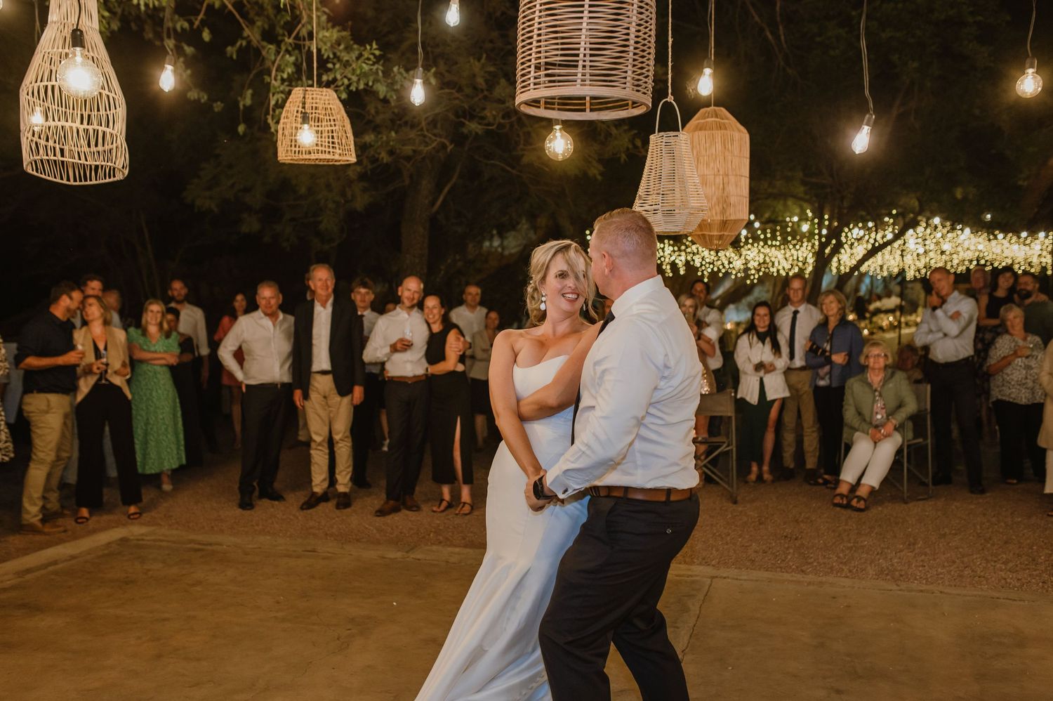 Outdoor wedding dance floor illuminated by hanging basket lanterns and Edison bulbs.