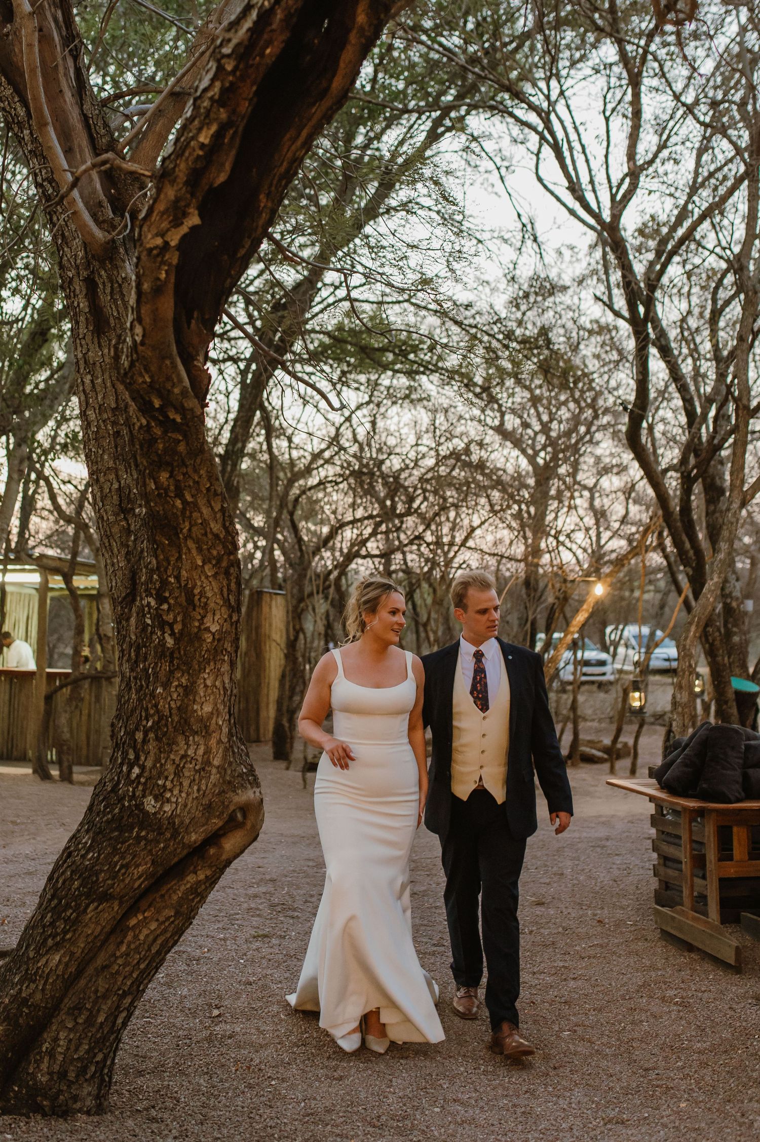 A couple walks through a rustic wooded area with twisted tree trunks.