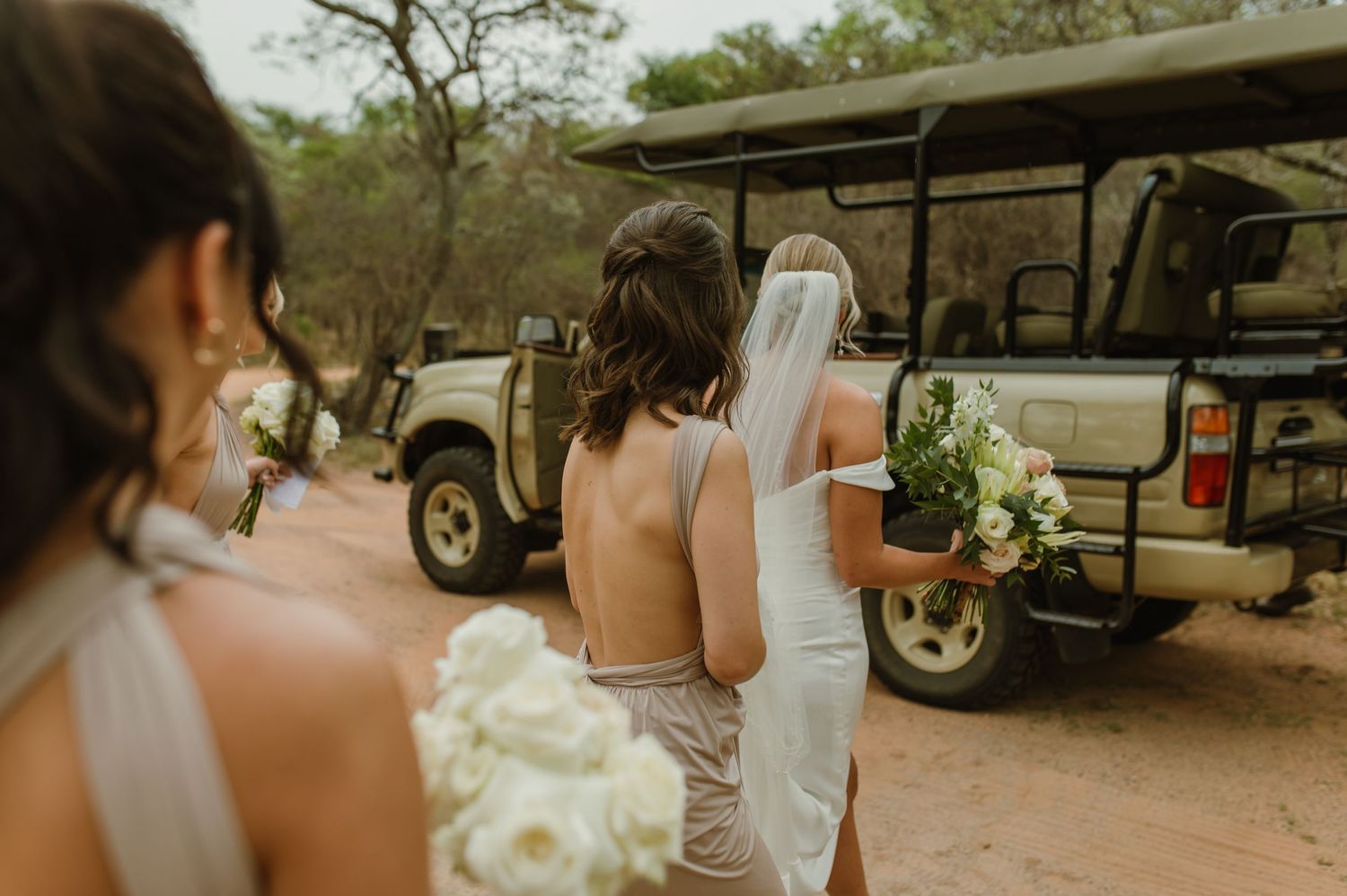 Wedding party gathered near vehicle in outdoor setting with bouquets.