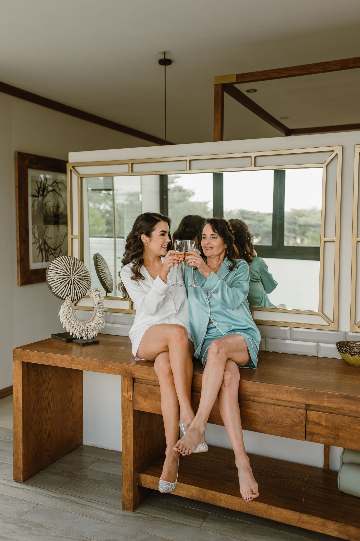 Friends sitting and laughing together on a rustic wooden bench in a modern room with large windows.