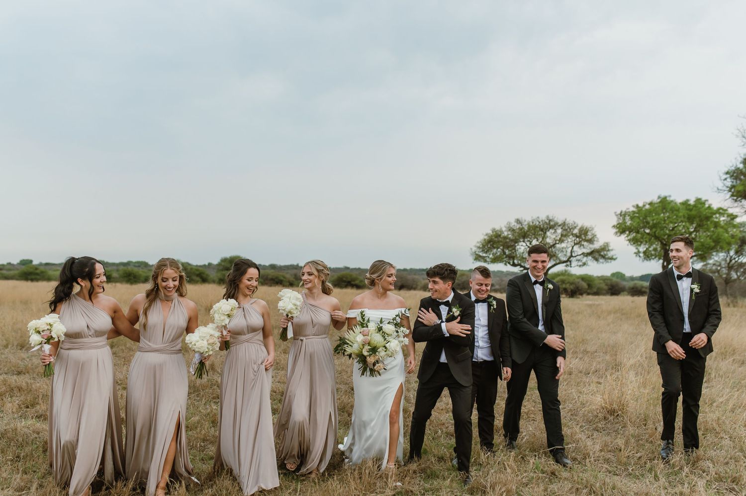 Wedding party members arranged in a row across an open field.