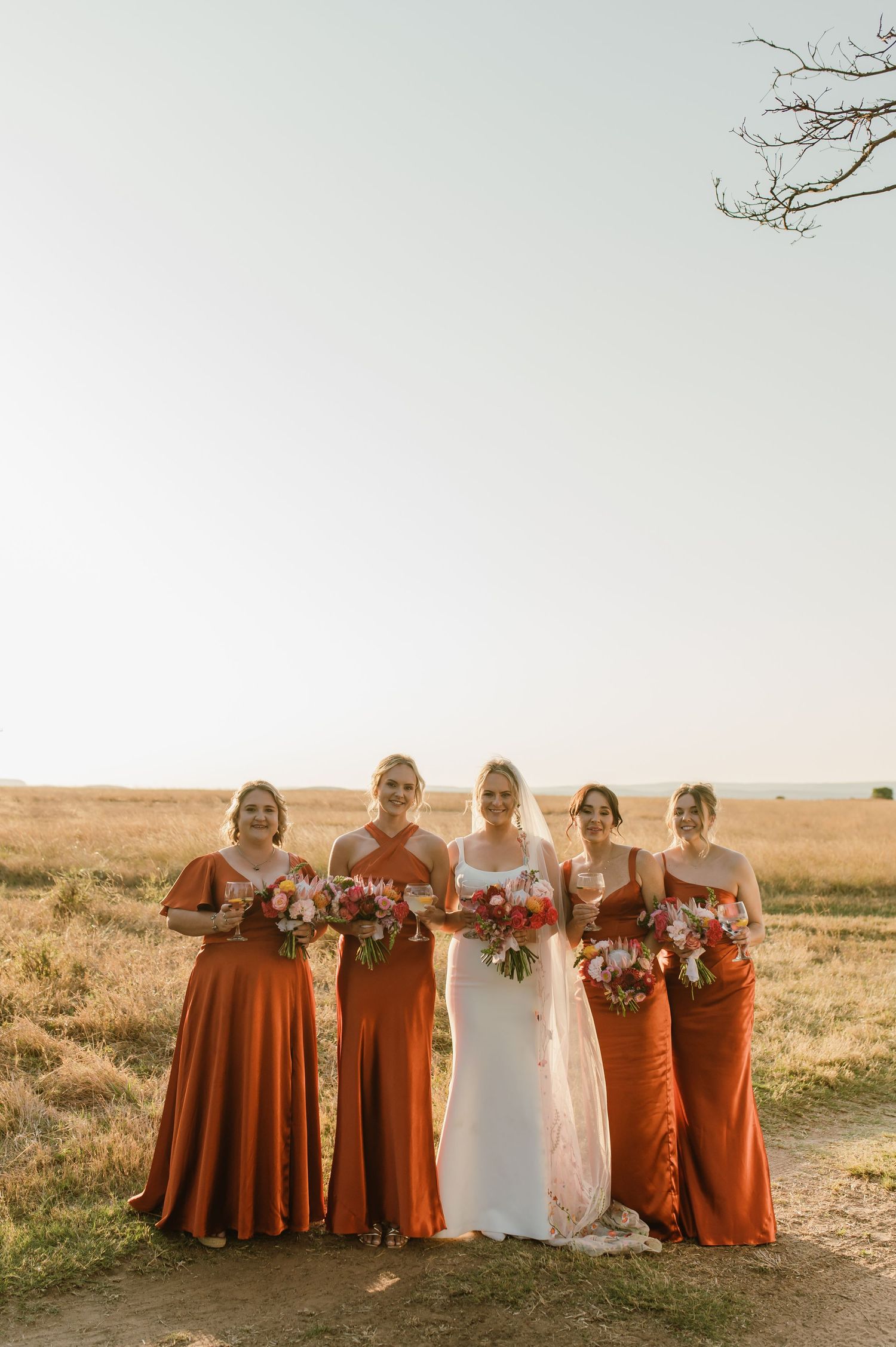 Wedding party in orange bridesmaid dresses poses together in a field at golden hour.