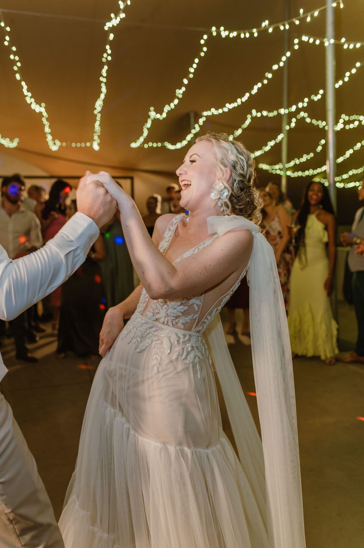 Person in white dress dancing joyfully beneath twinkling reception lights.