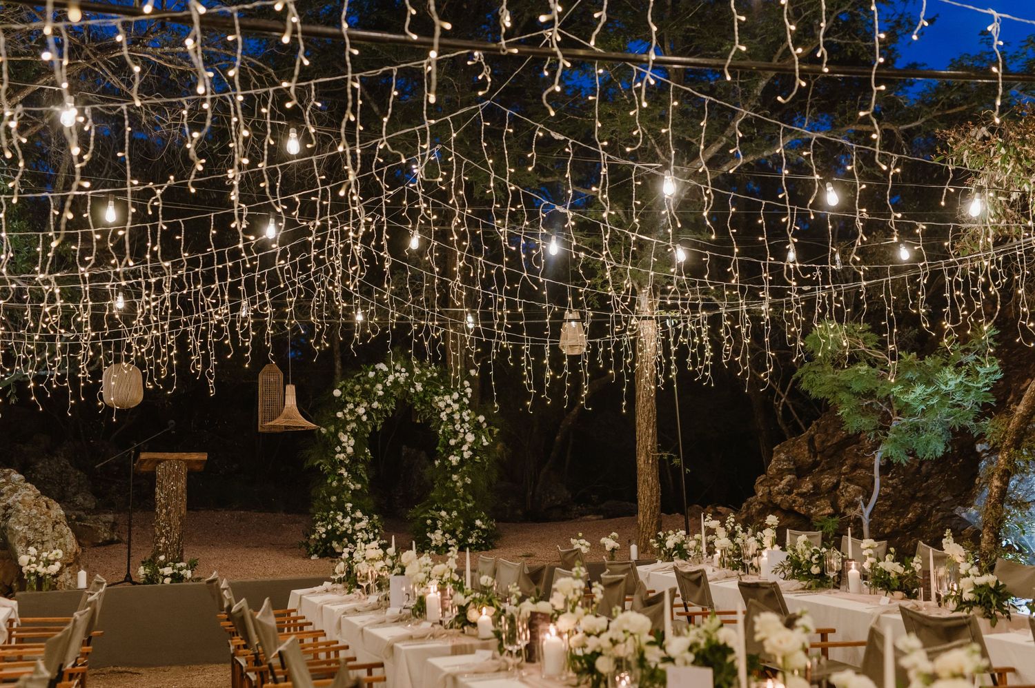 Enchanting outdoor wedding reception setup with hanging string lights creating a magical canopy overhead.