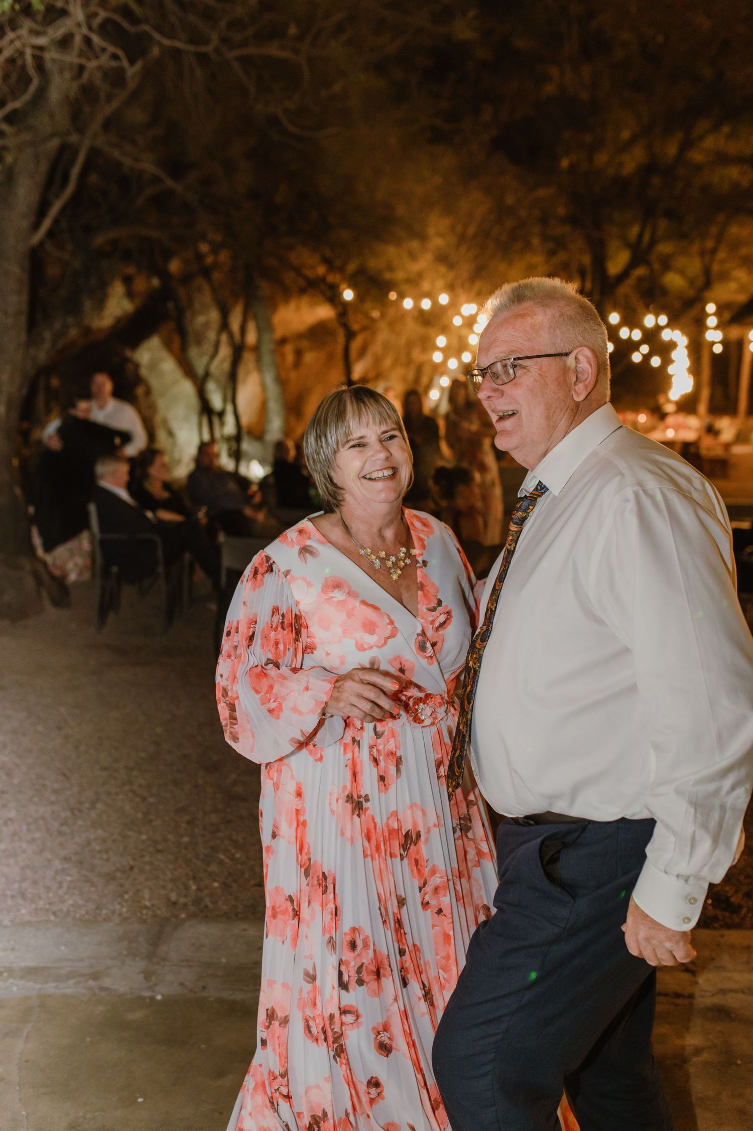 Couples dancing together at an evening wedding celebration with twinkle lights in the background.