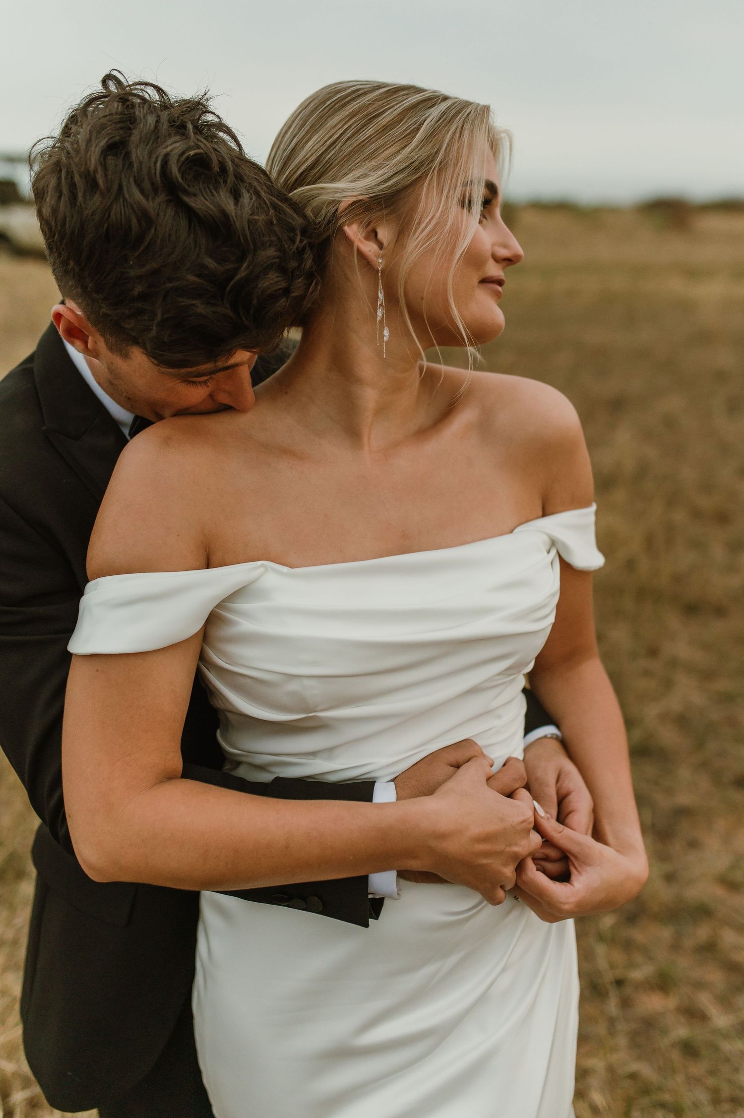 Intimate wedding moment captured as couple embraces in an outdoor field setting.