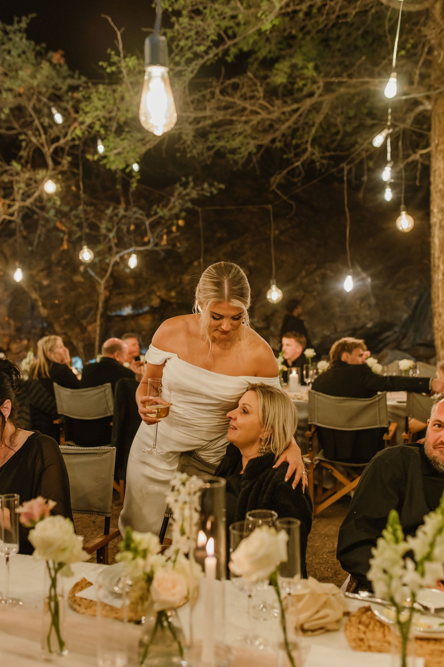 Elegant outdoor wedding reception with guests dining under illuminated string lights.